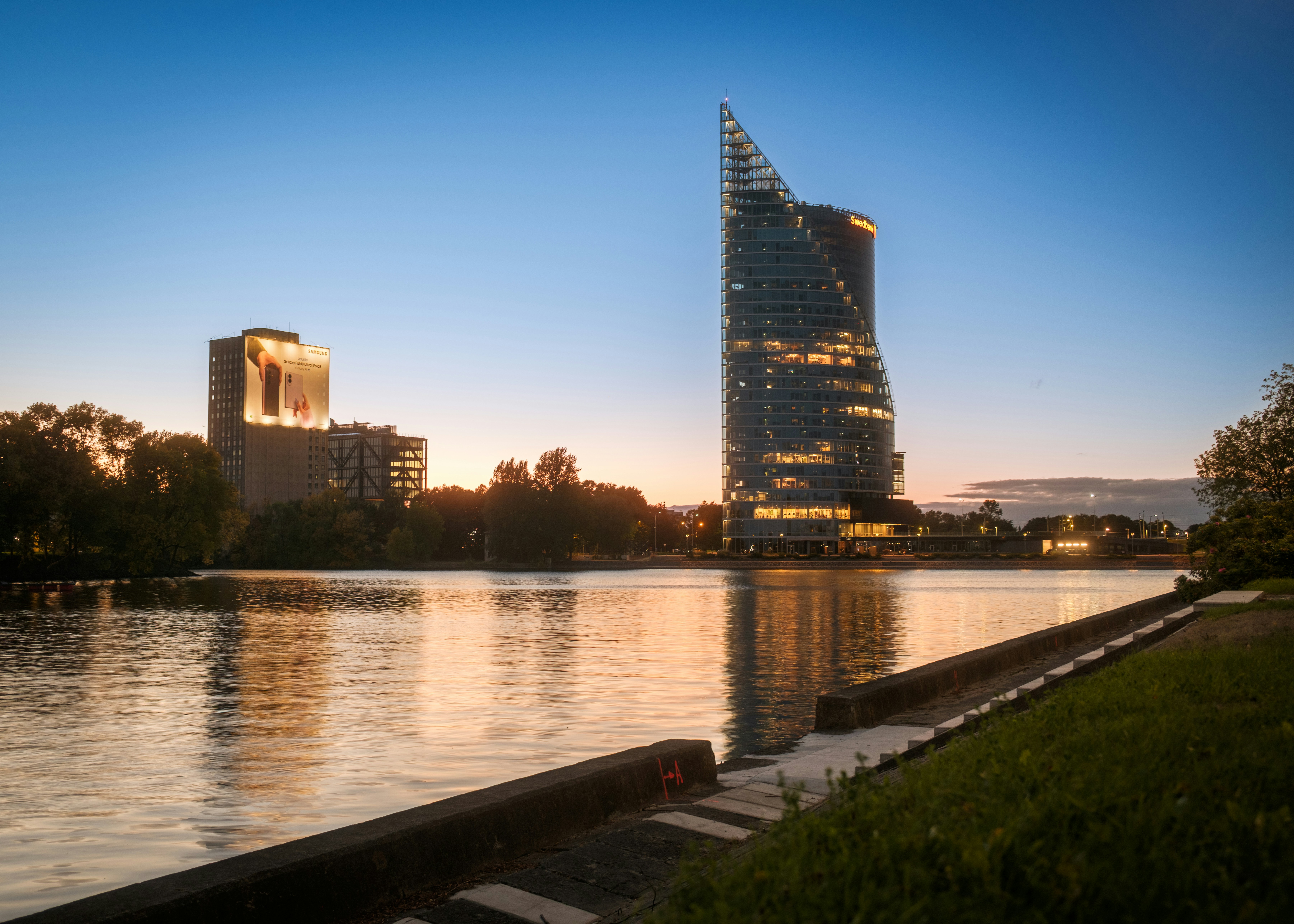 A modern curved skyscraper and a tall building by a river at twilight