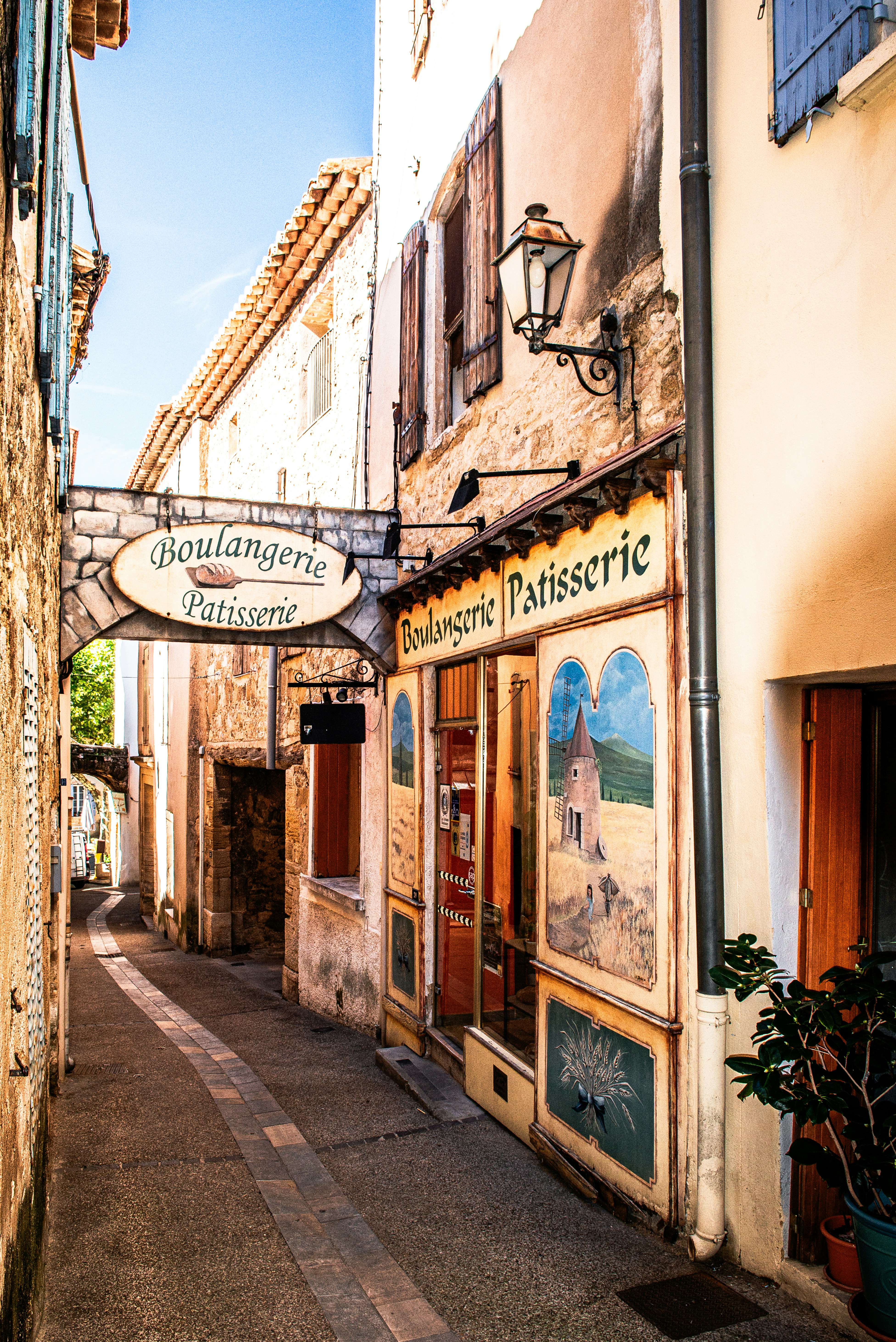 A narrow stone street with a boulangerie patisserie shop featuring painted murals on its facade