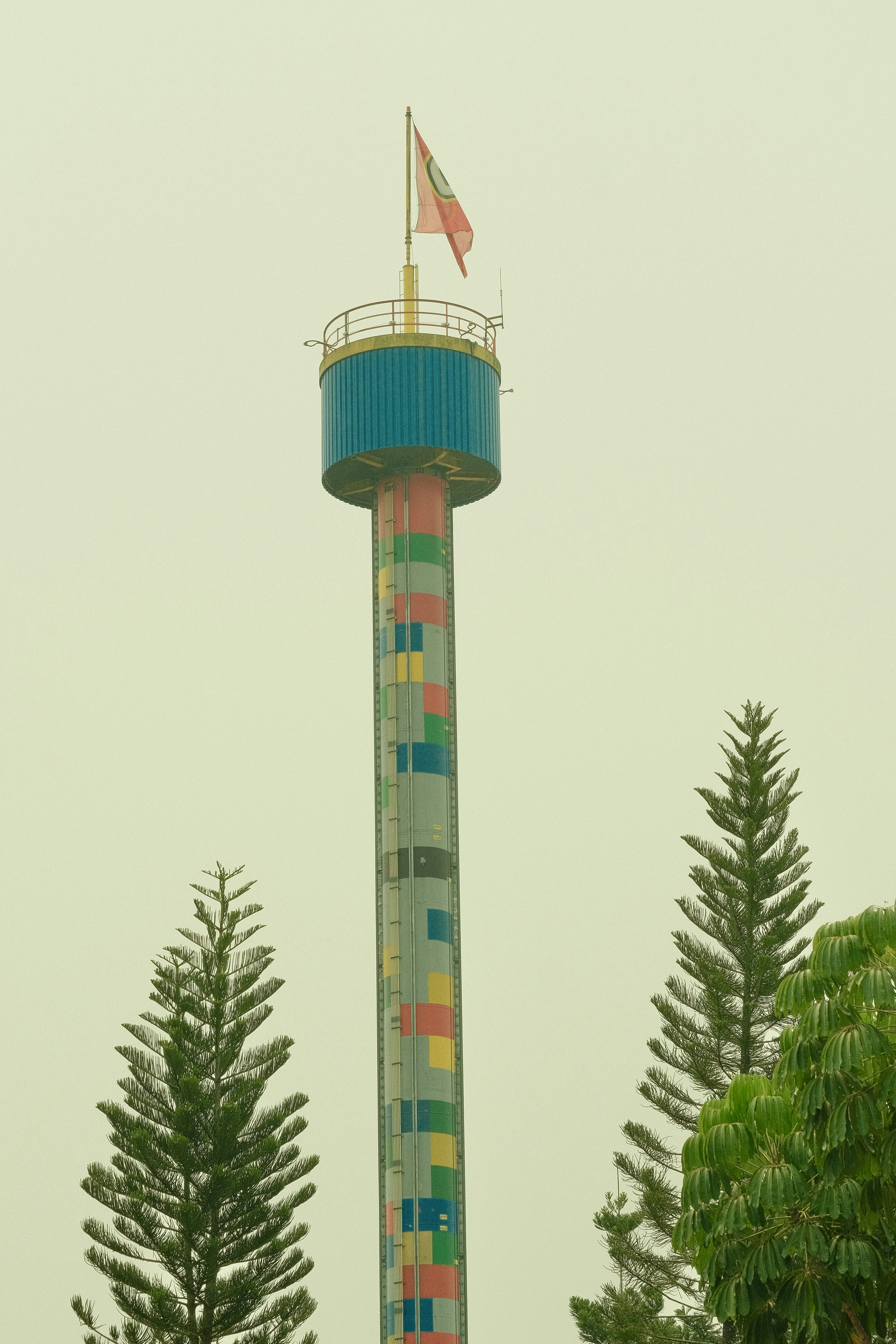 A tall observation tower with a colorful patterned shaft between two evergreen trees