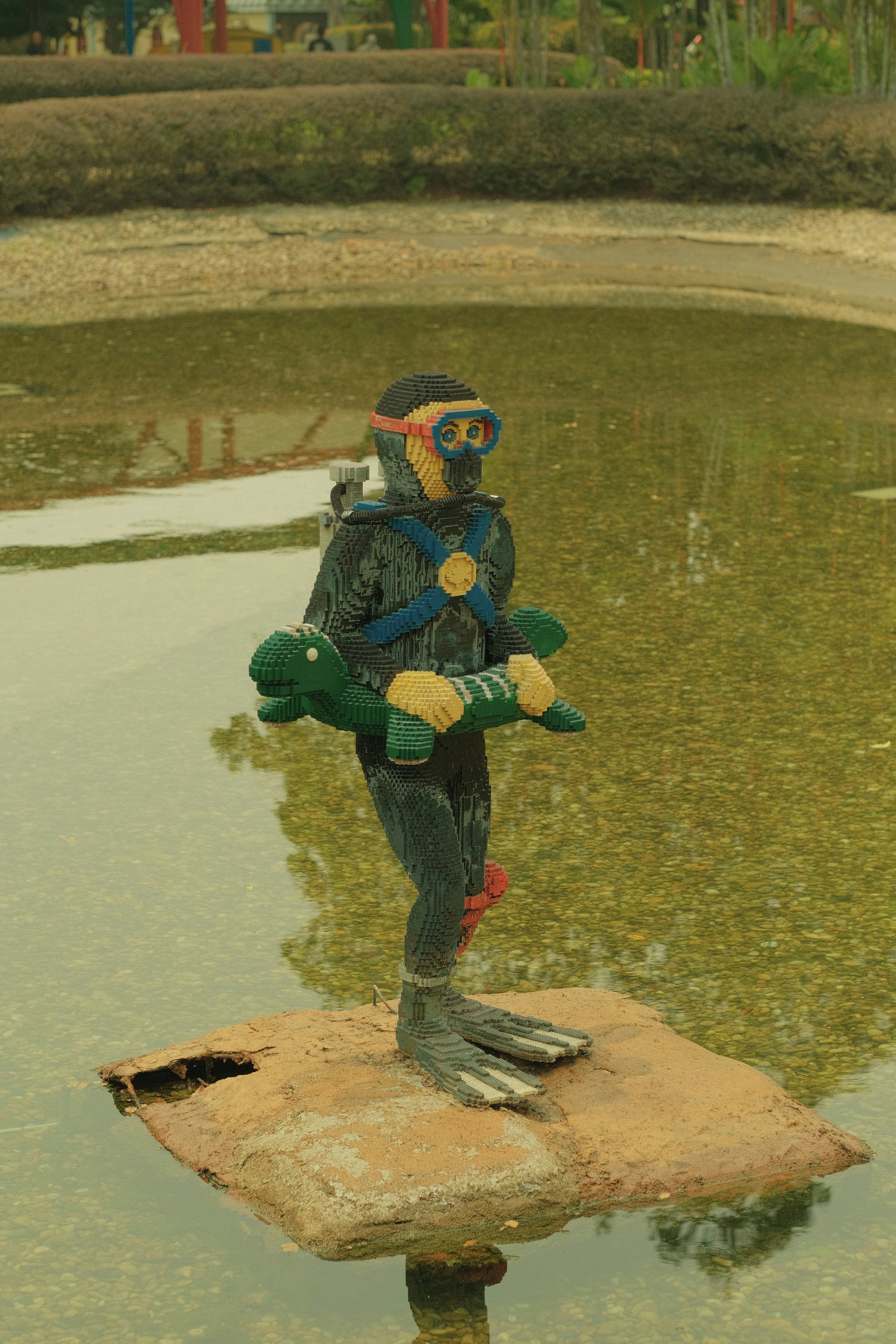 A Lego diver figure holding a green sea turtle in a shallow pond