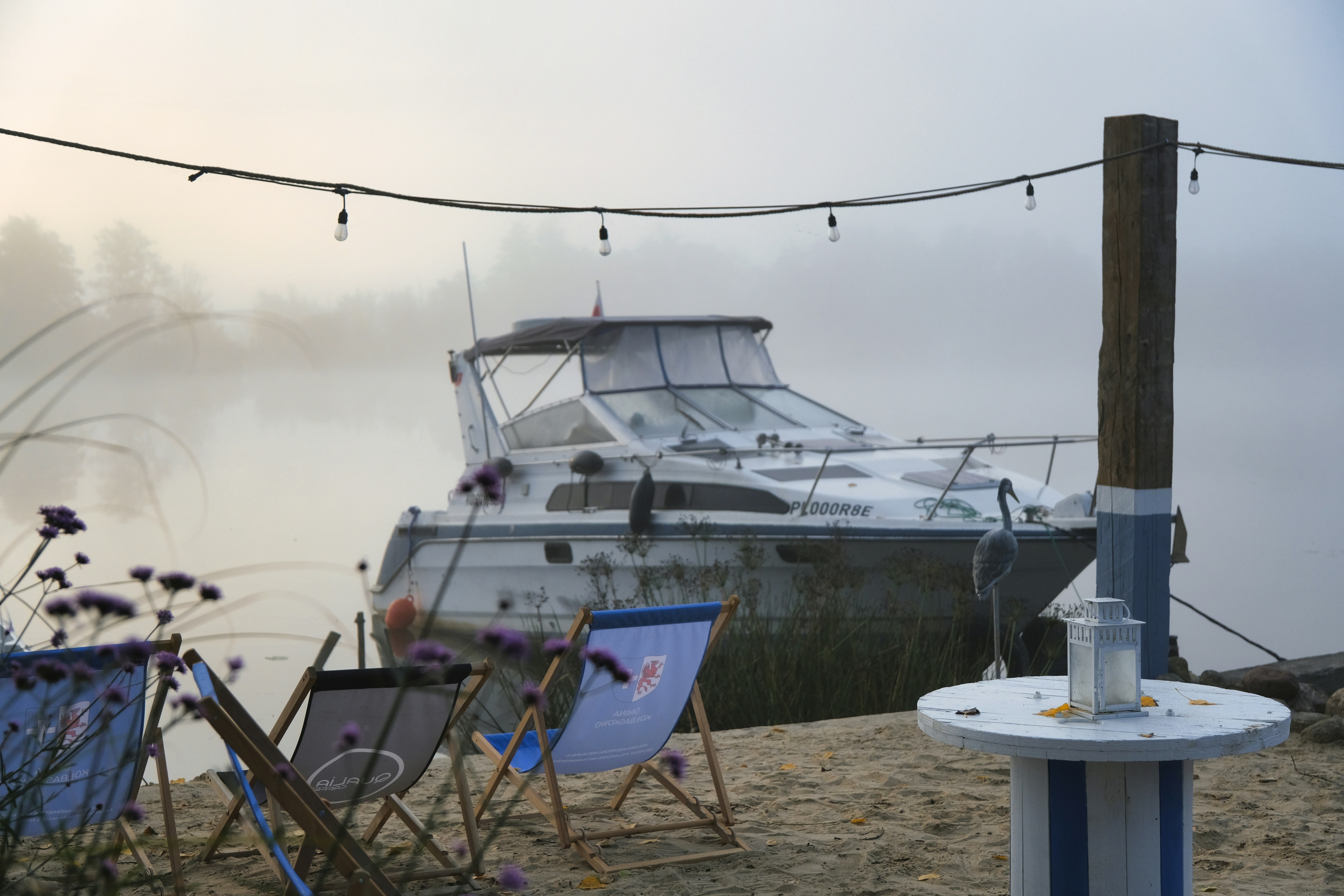 A motorboat moored at a sandy shore in misty conditions with deck chairs