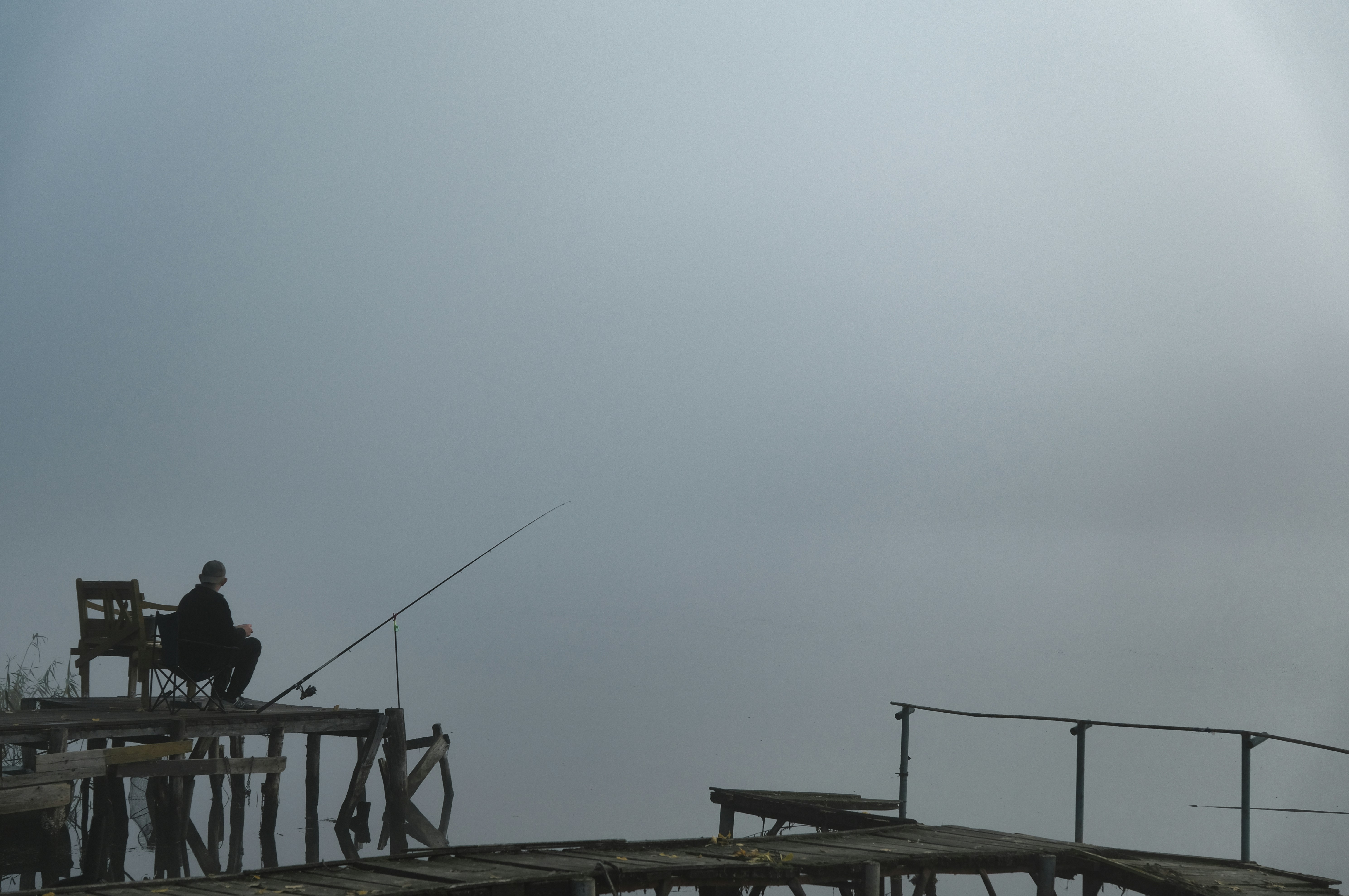 A person fishing from a wooden pier into a thick misty lake