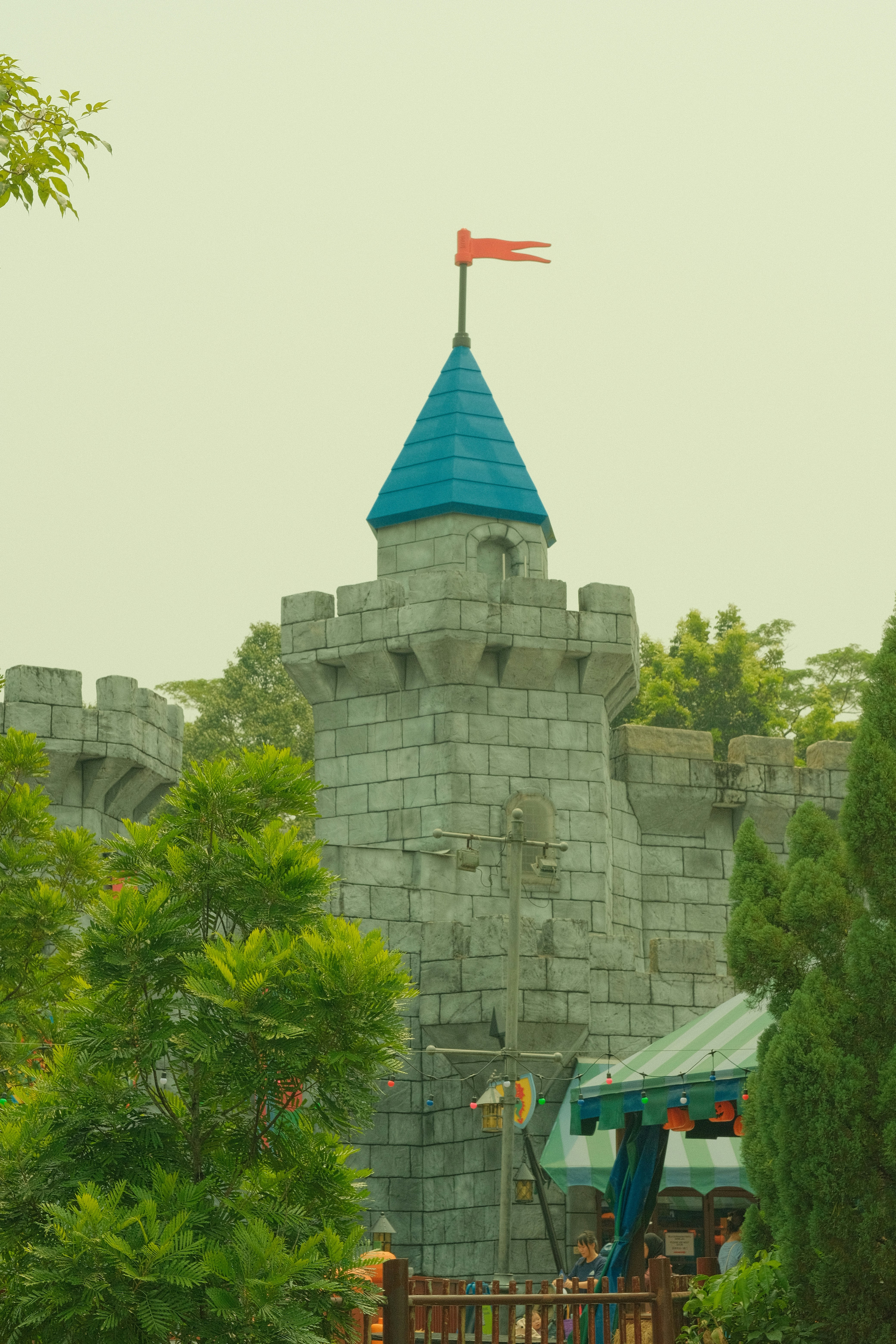 A stone castle tower with a blue roof and red flag among trees