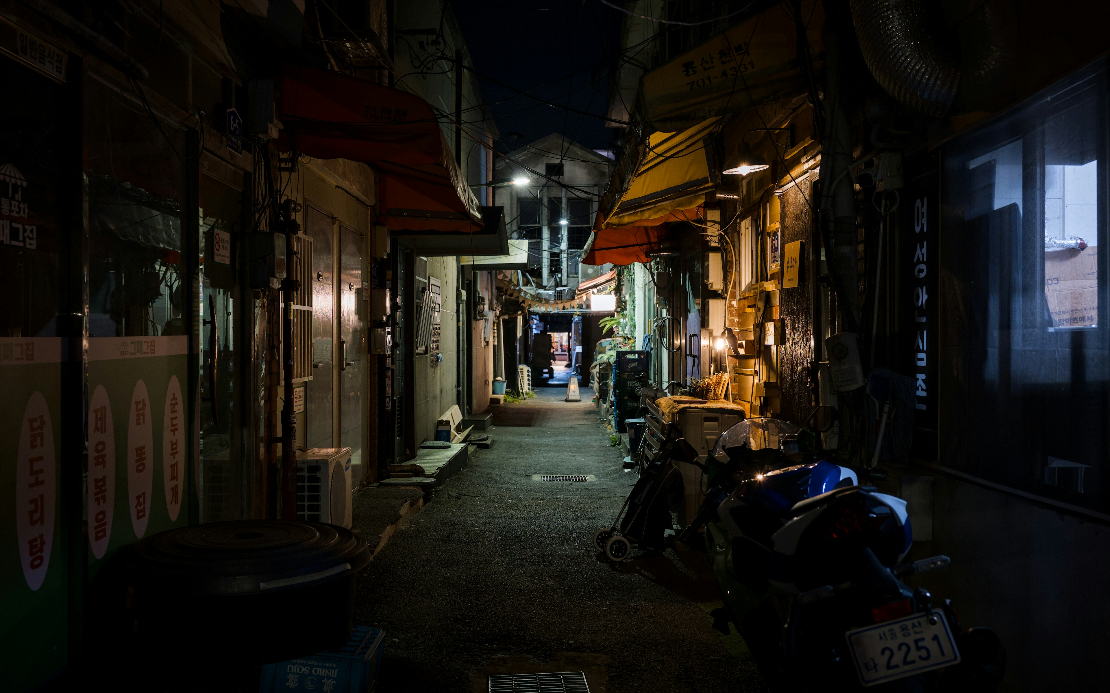 A narrow alleyway at night with a parked motorcycle and yellow fabric awnings