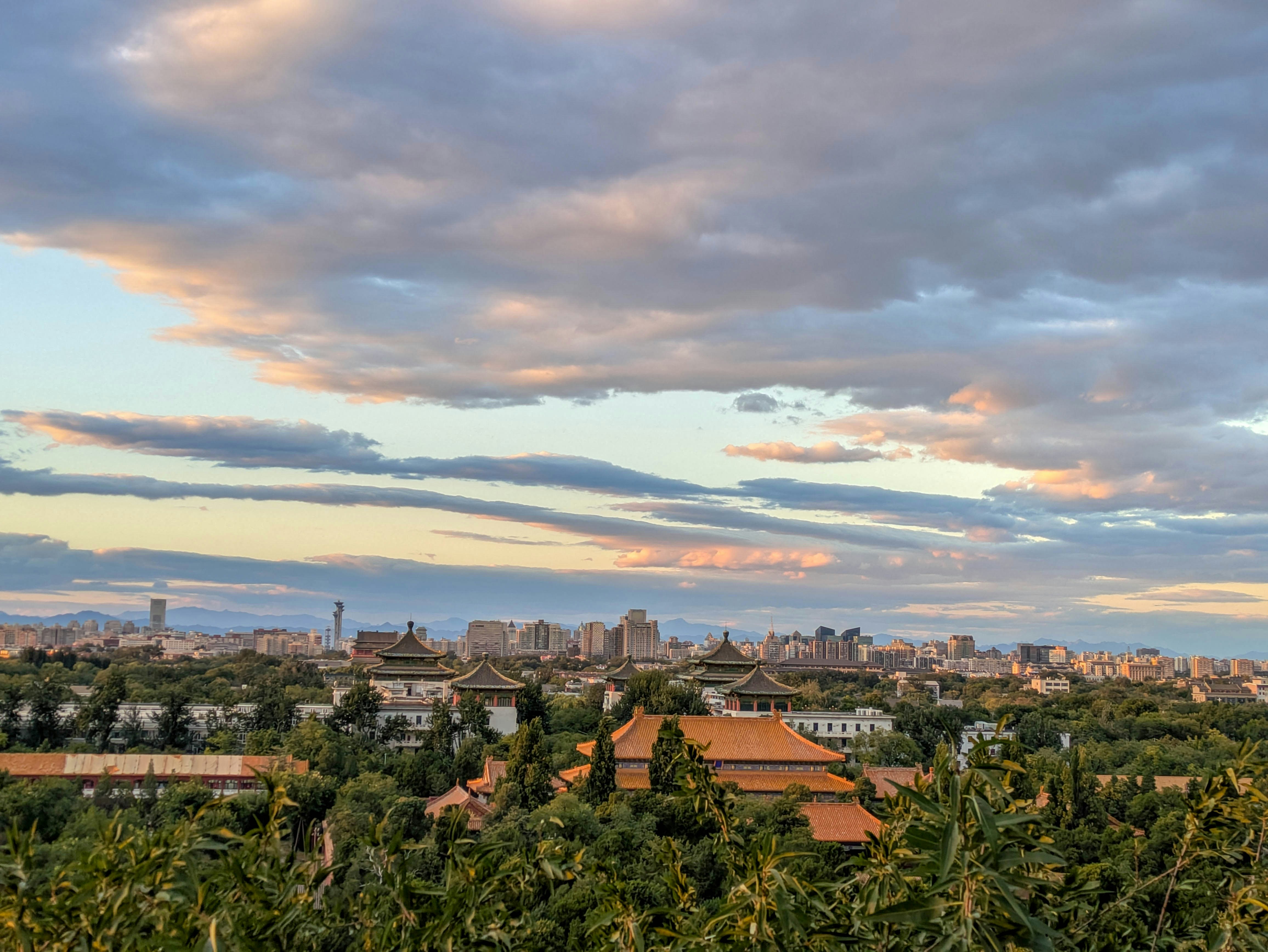 Traditional Chinese architecture with orange roofs nestled in lush greenery under a cloudy sky