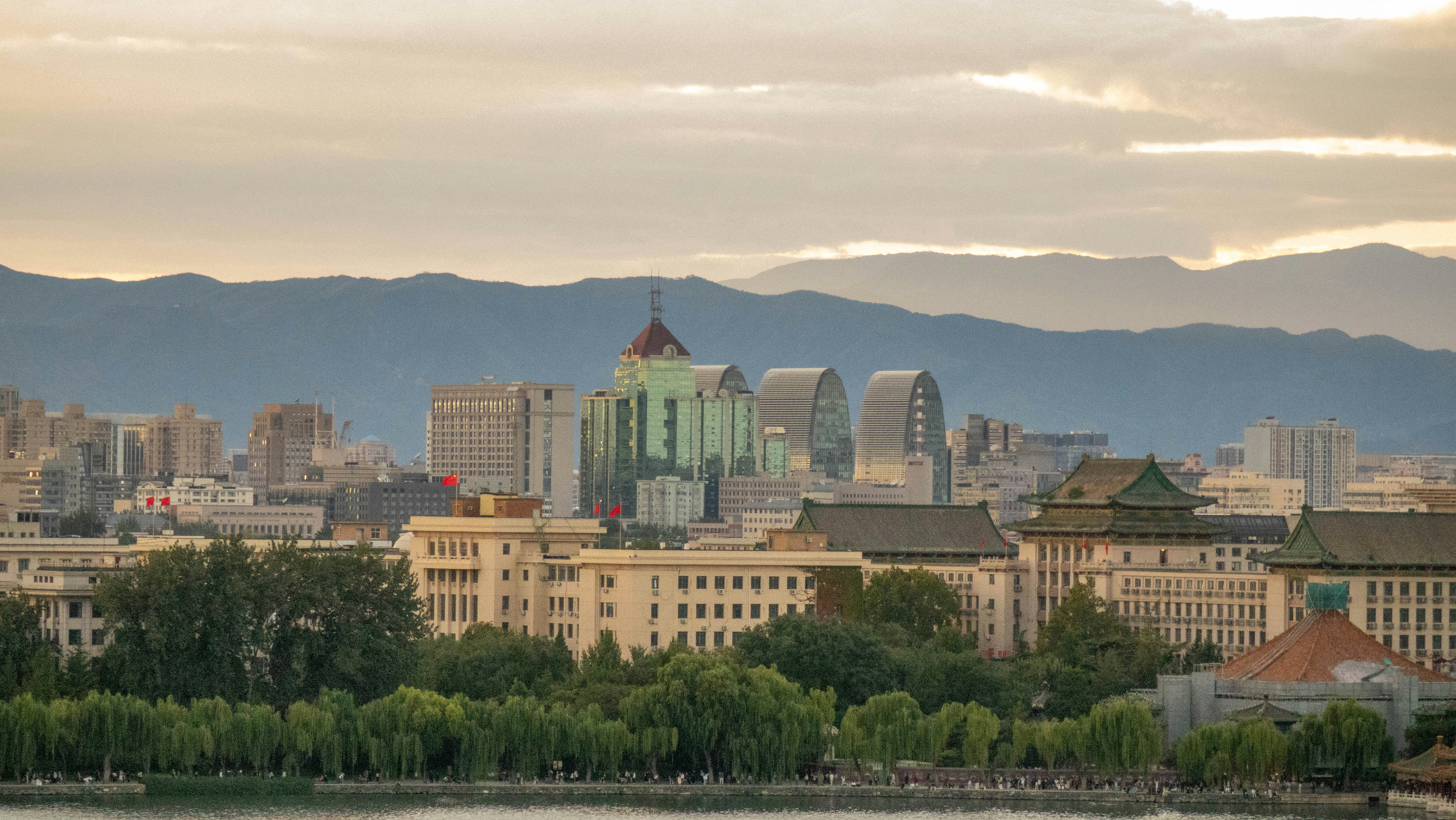 A city skyline with traditional and modern buildings before distant mountains at golden hour