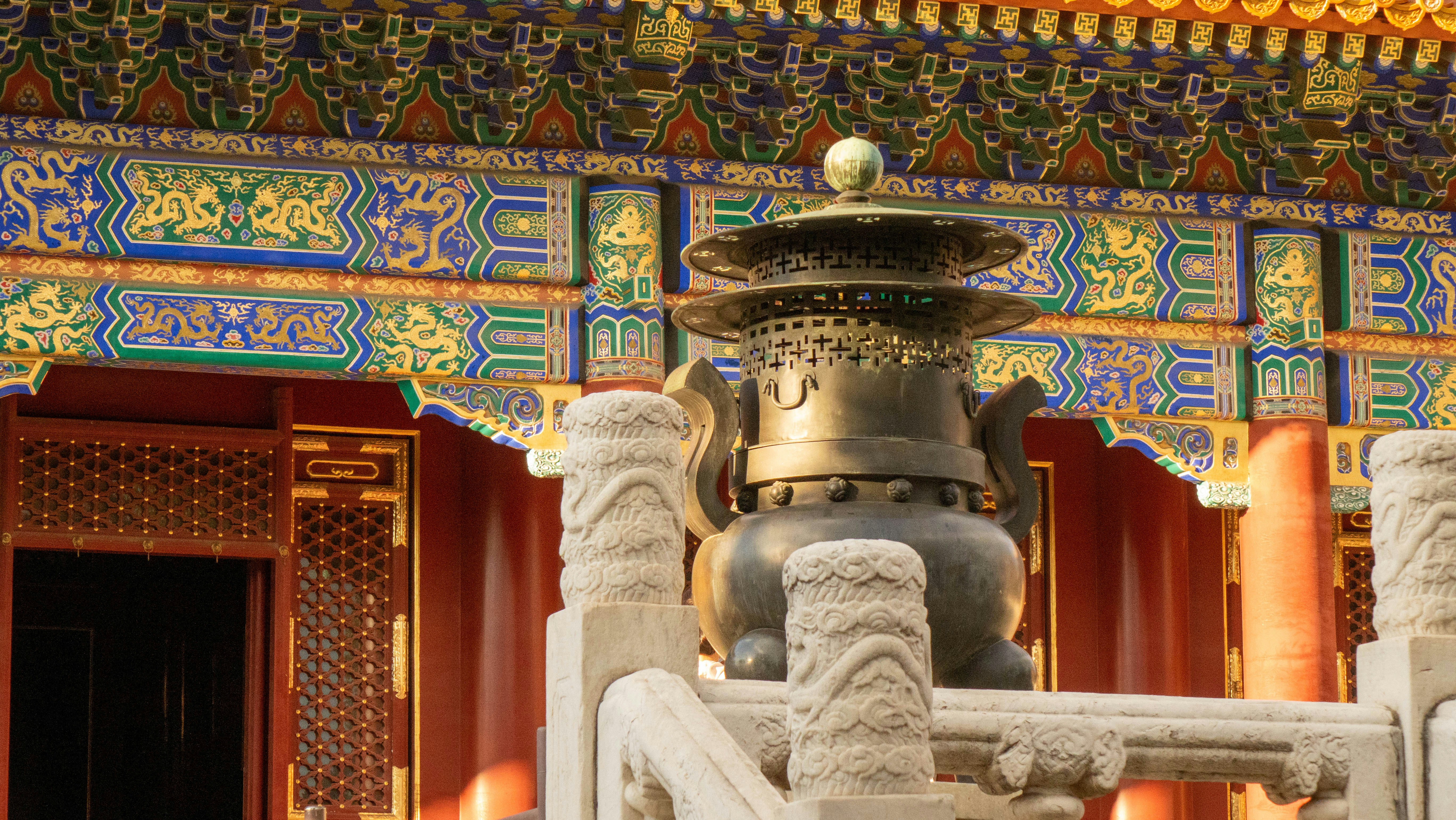 A bronze incense burner on a stone balustrade before an ornate building in Beijing