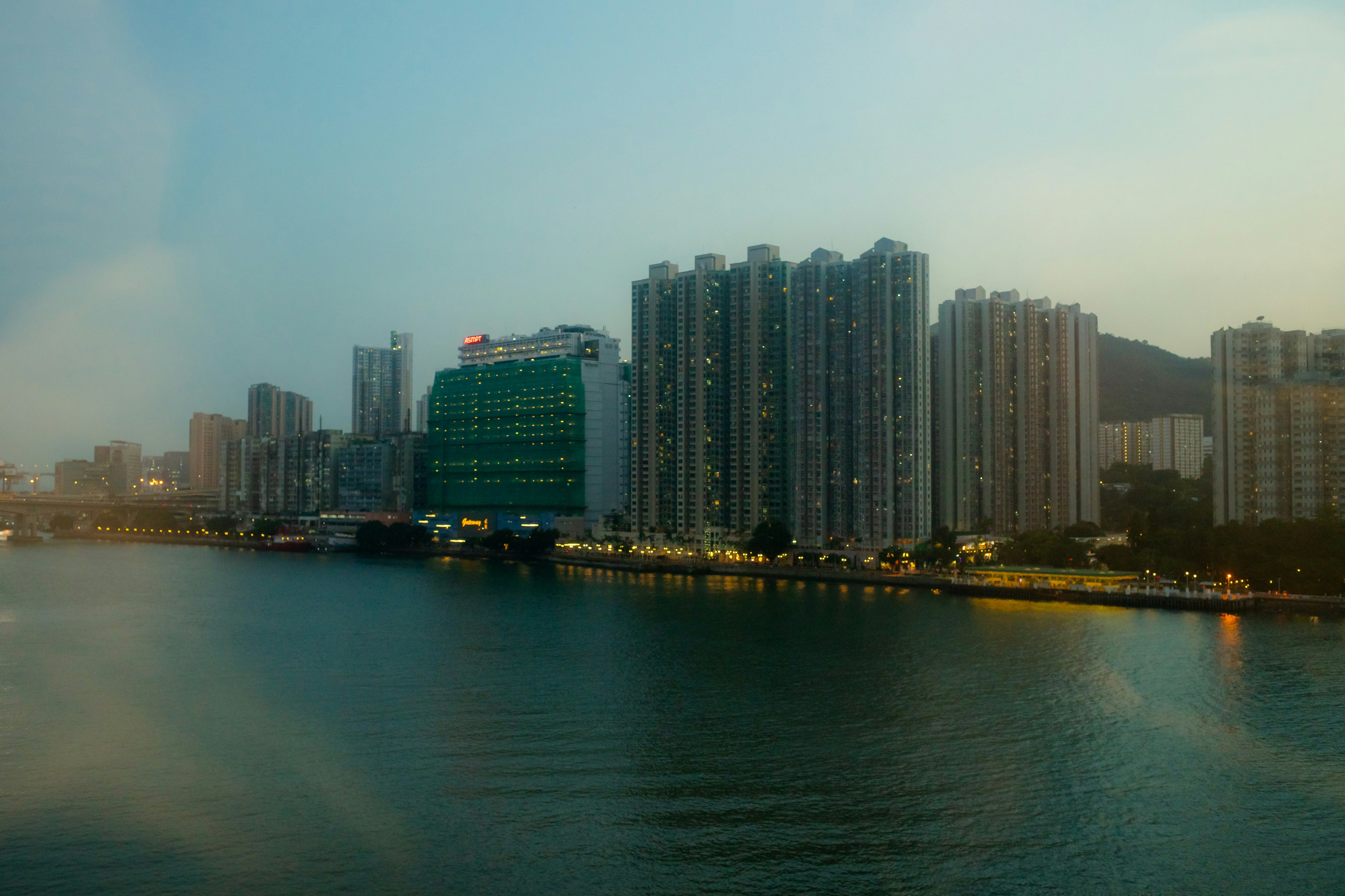 Tall residential apartment buildings along a waterfront at dusk with warm glowing lights