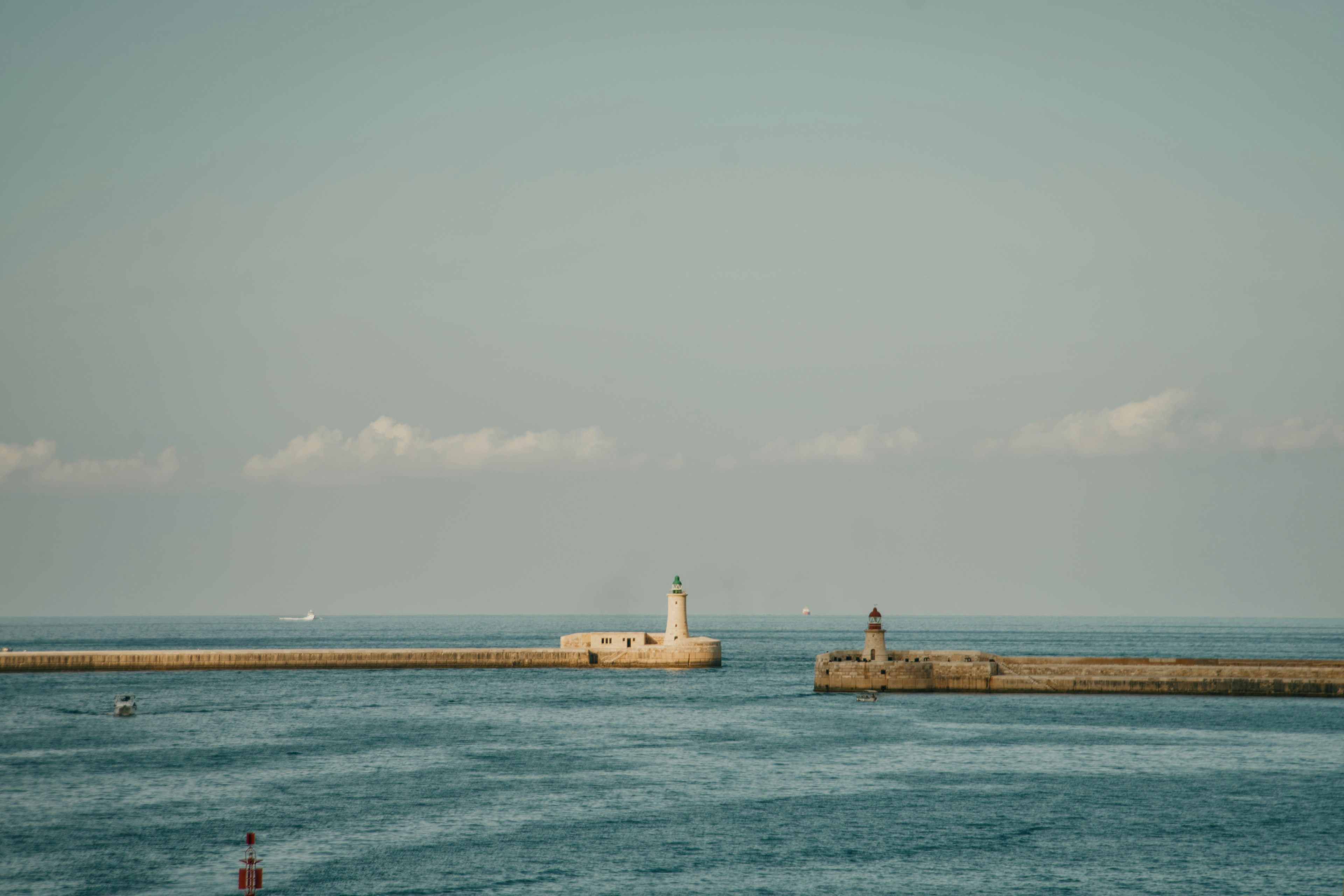Two stone breakwaters with lighthouses at the entrance to a calm blue harbor