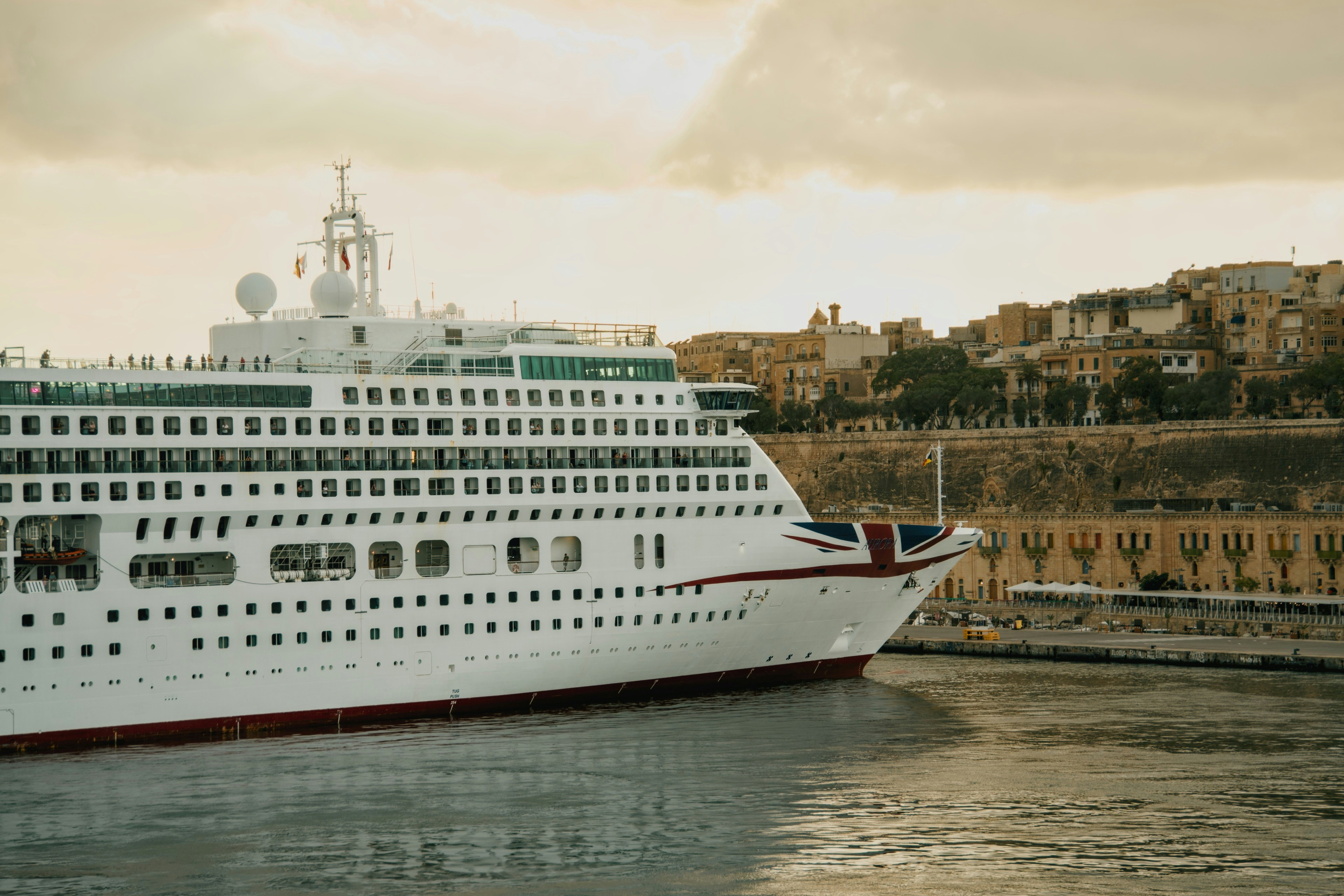A large white cruise ship with a Union Jack bow design near a stone city