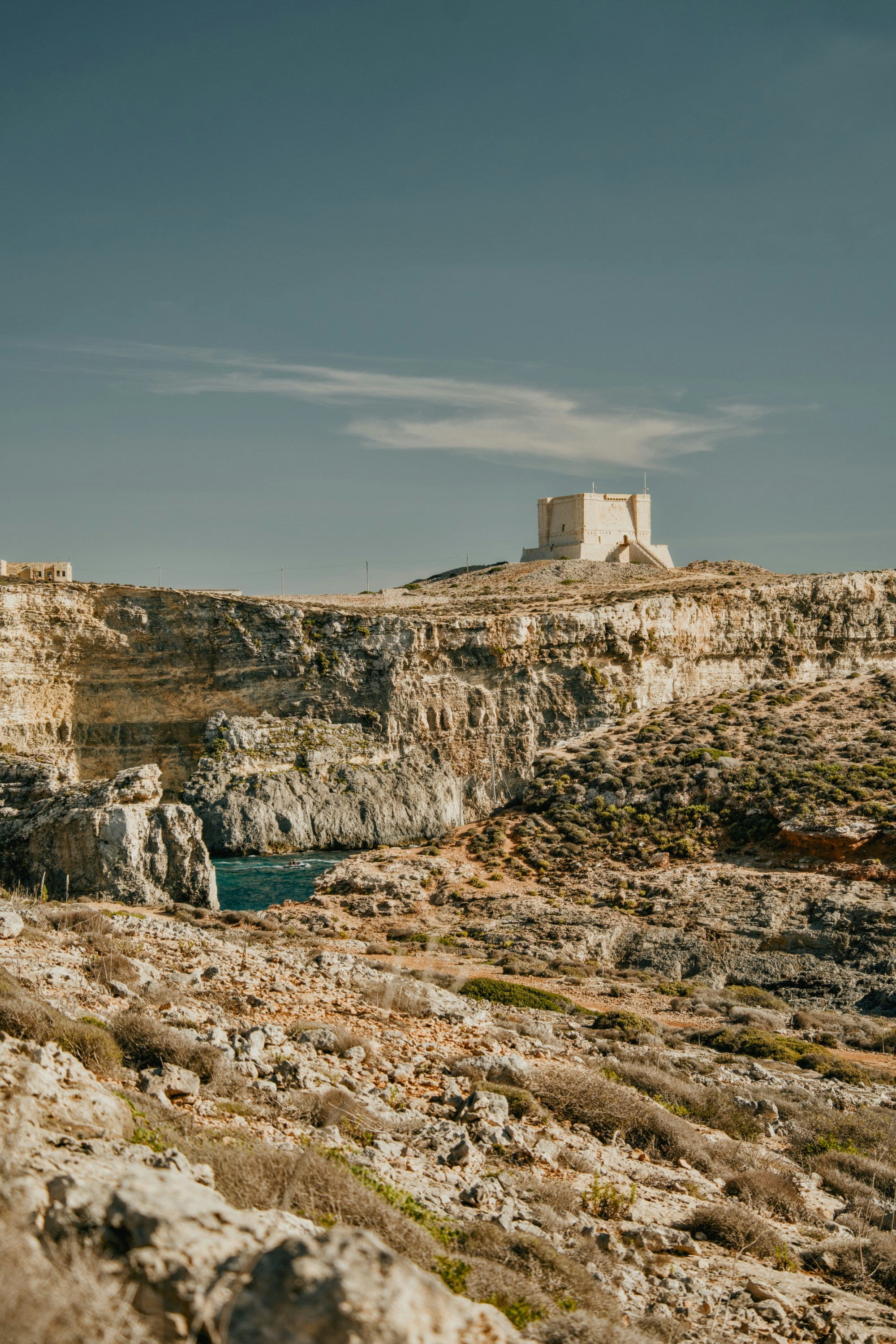 A stone watchtower on a rocky cliff overlooking a blue sea inlet