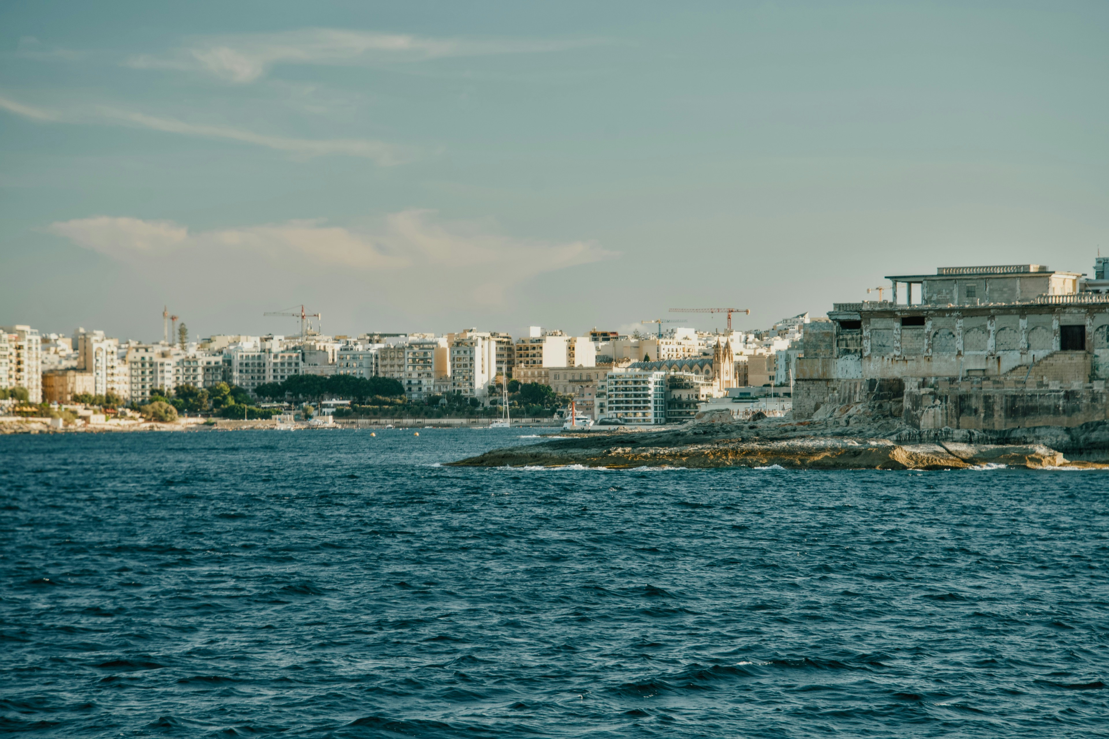 A coastal city skyline with stone ruins on a rocky point above the sea
