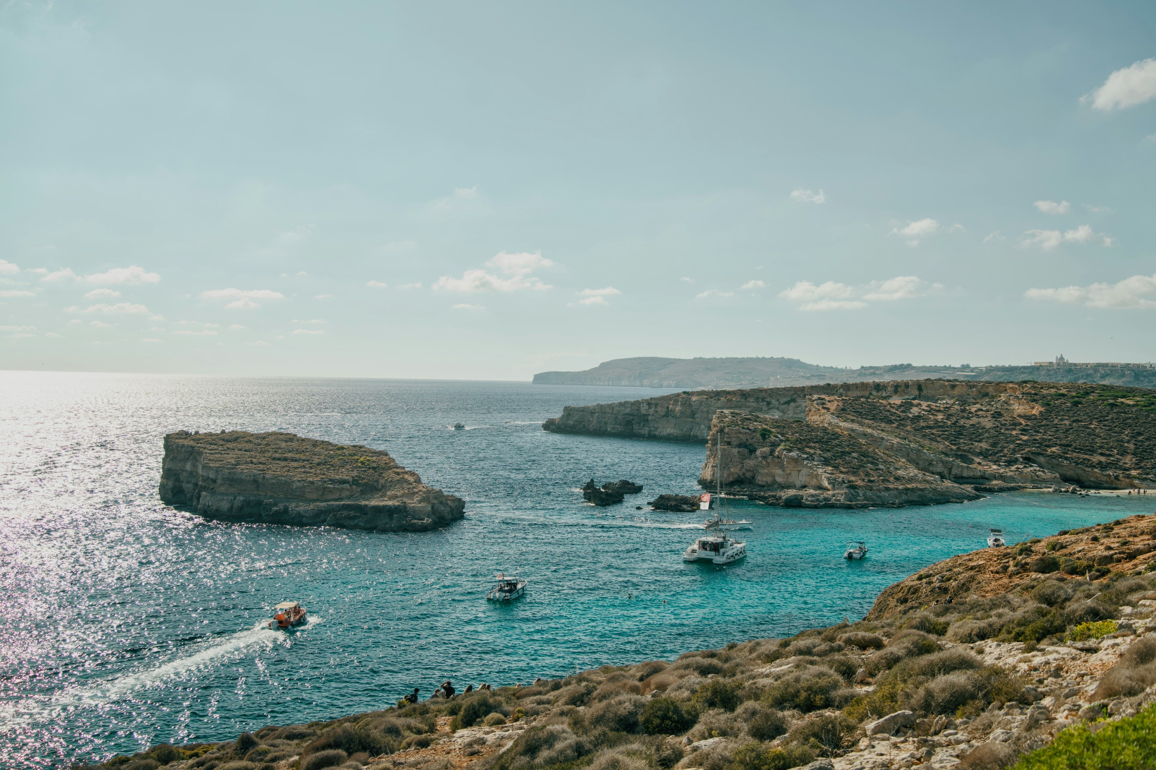 Small boats on turquoise water between rocky cliffs under a bright blue sky