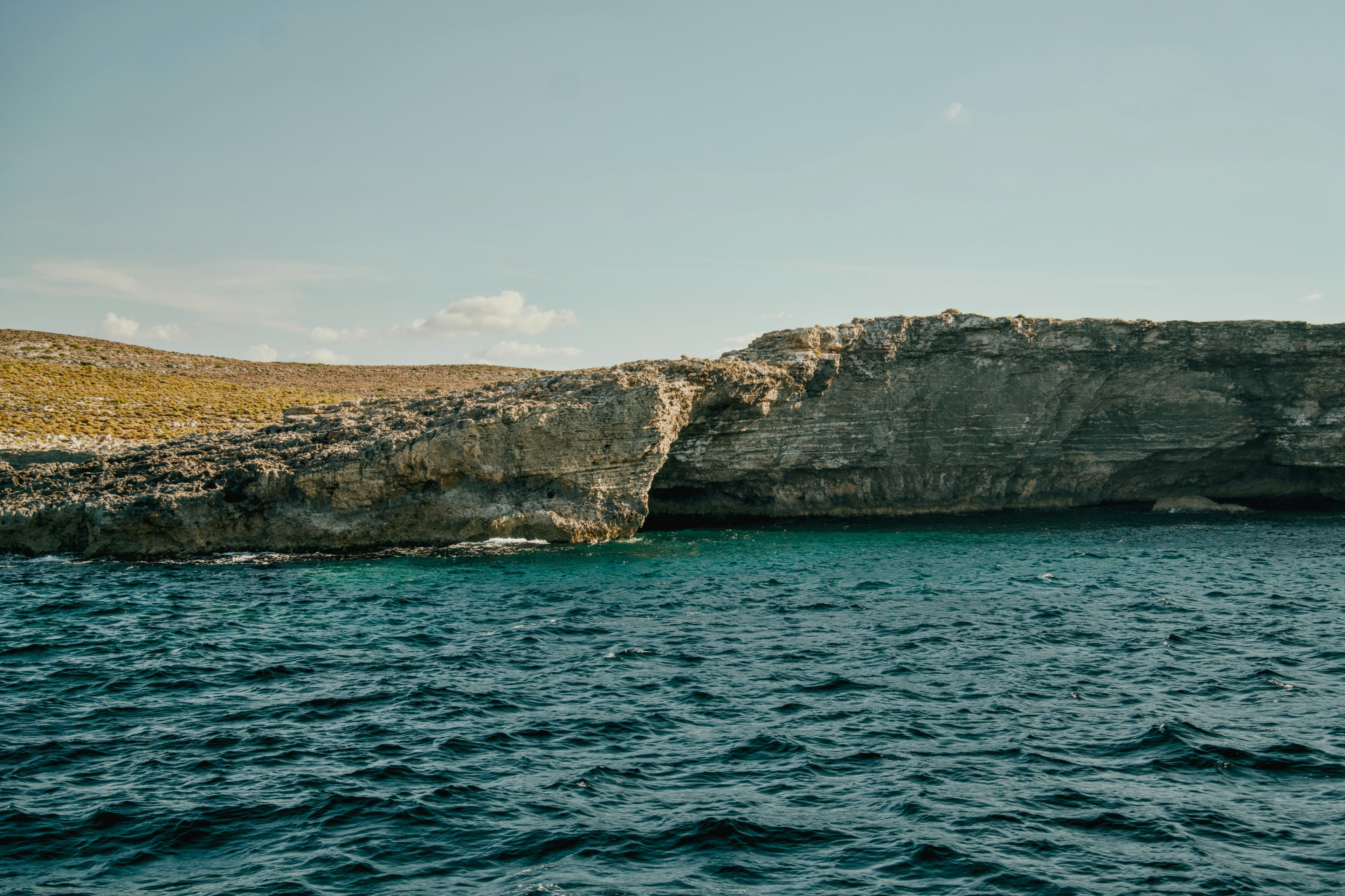 A rocky cliff with a natural arch above deep blue sea water