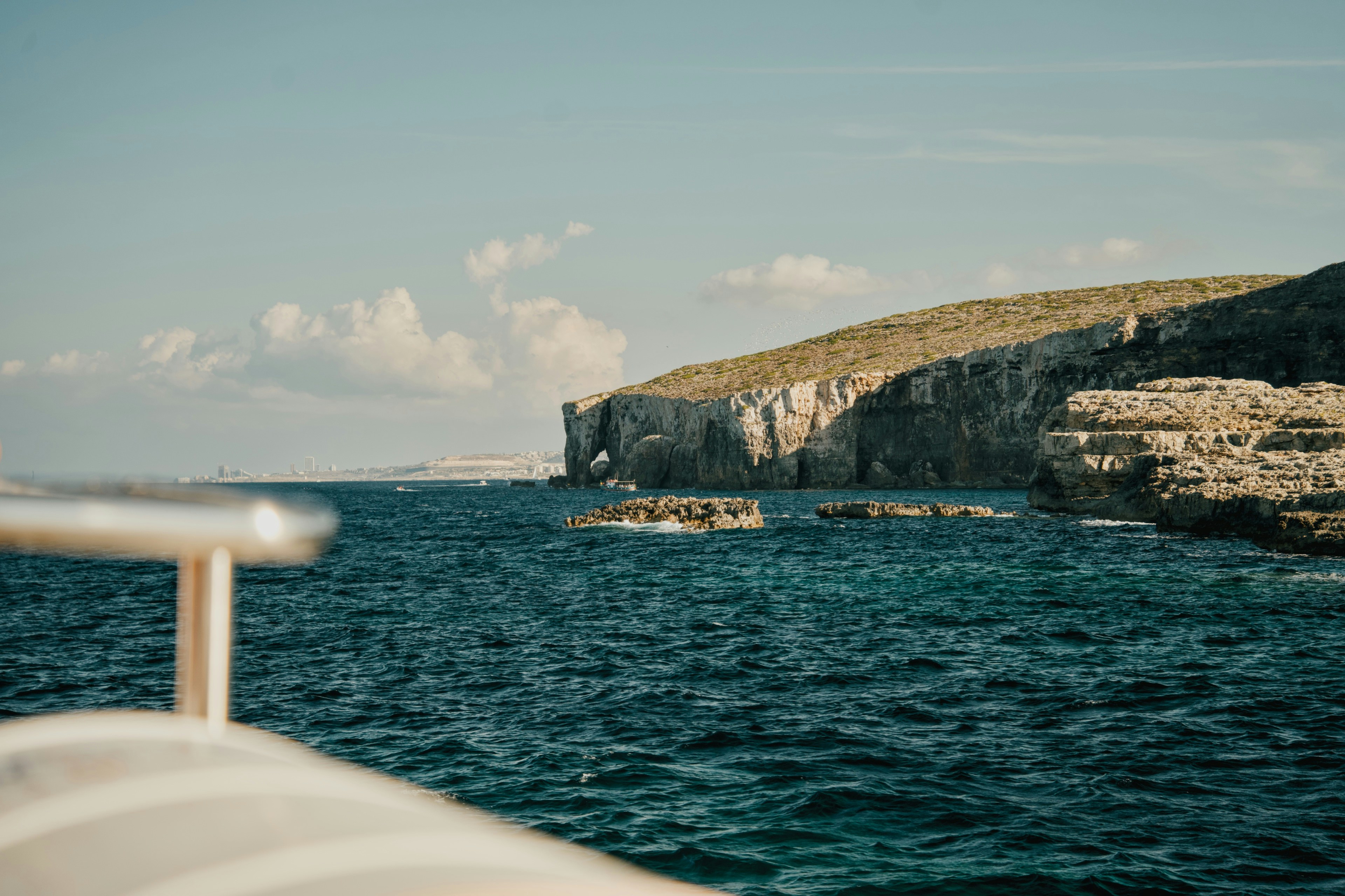 A rocky cliff with a natural arch above deep blue sea water