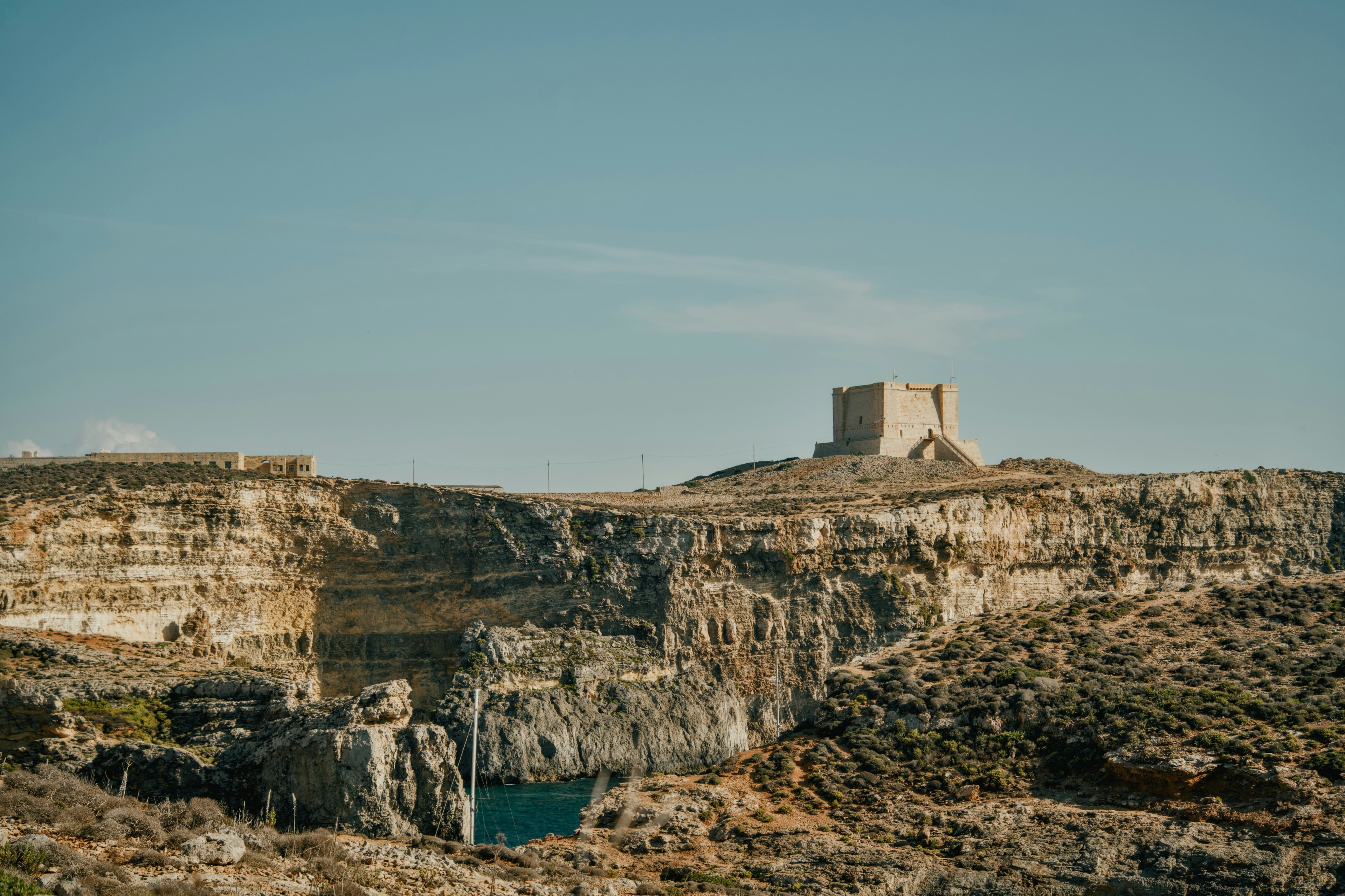 A stone watchtower on a rocky cliff overlooking a deep blue sea inlet