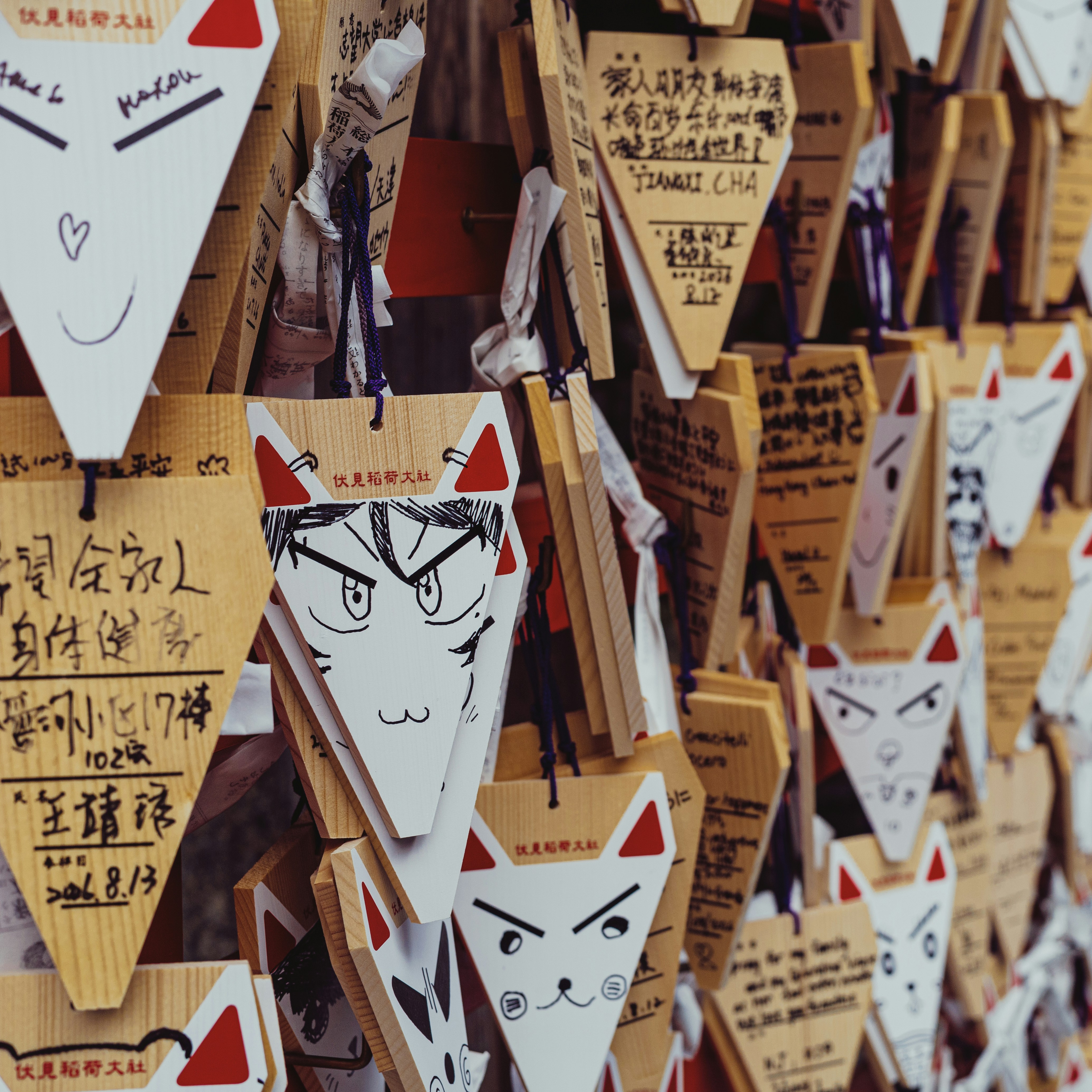Fox-shaped wooden ema prayer plaques with hand-drawn faces hanging at Fushimi Inari Shrine