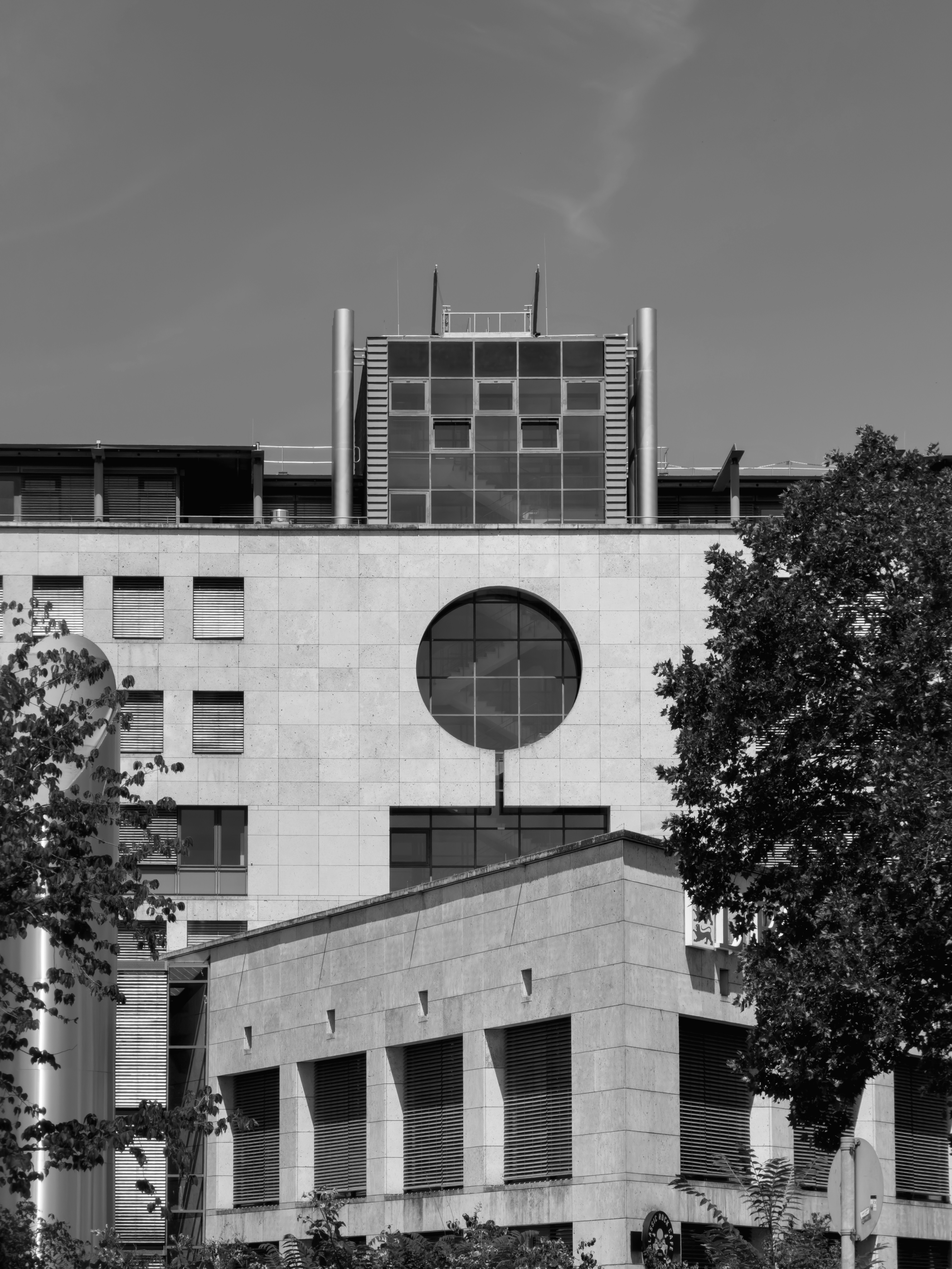 Ein modernes Steingebäude mit rundem Fenster, eingerahmt von Bäumen in Schwarz-Weiß