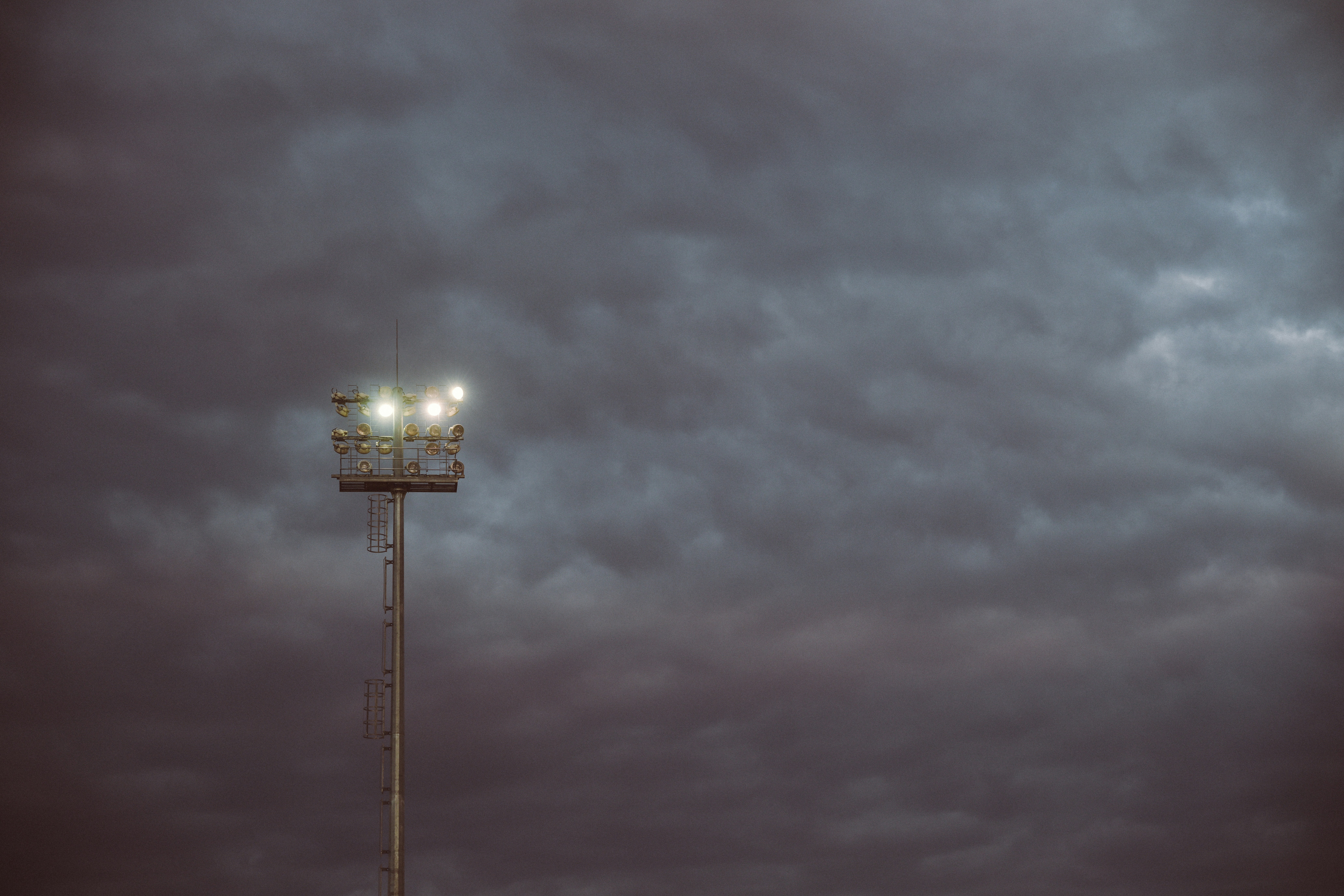 A tall stadium light tower glowing against a dark and cloudy night sky