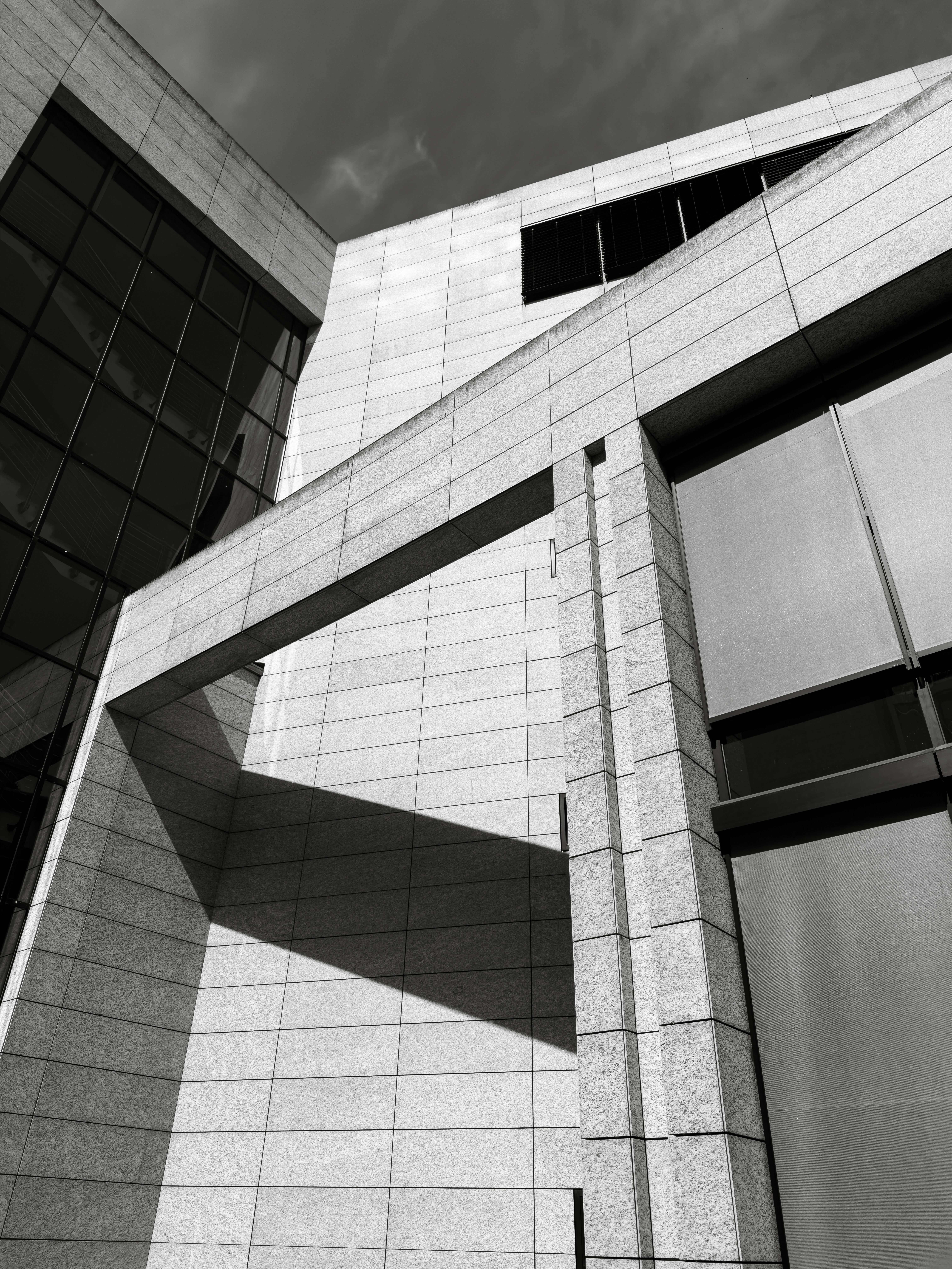 Eine moderne Gebäudefassade mit Steinziegeln, Glasfenstern und scharfen geometrischen Schatten