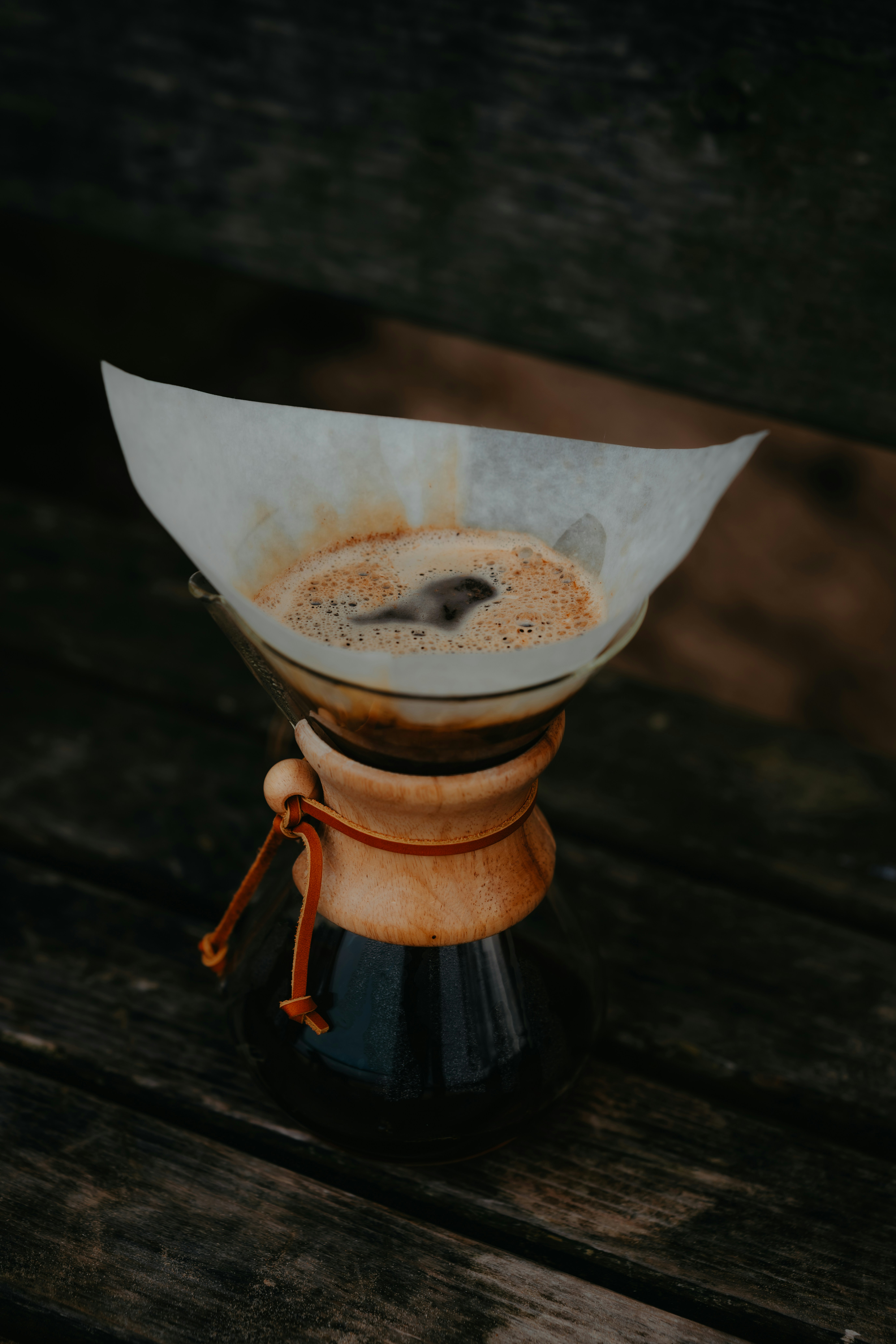 A glass pour-over coffee maker with a paper filter on a wooden surface