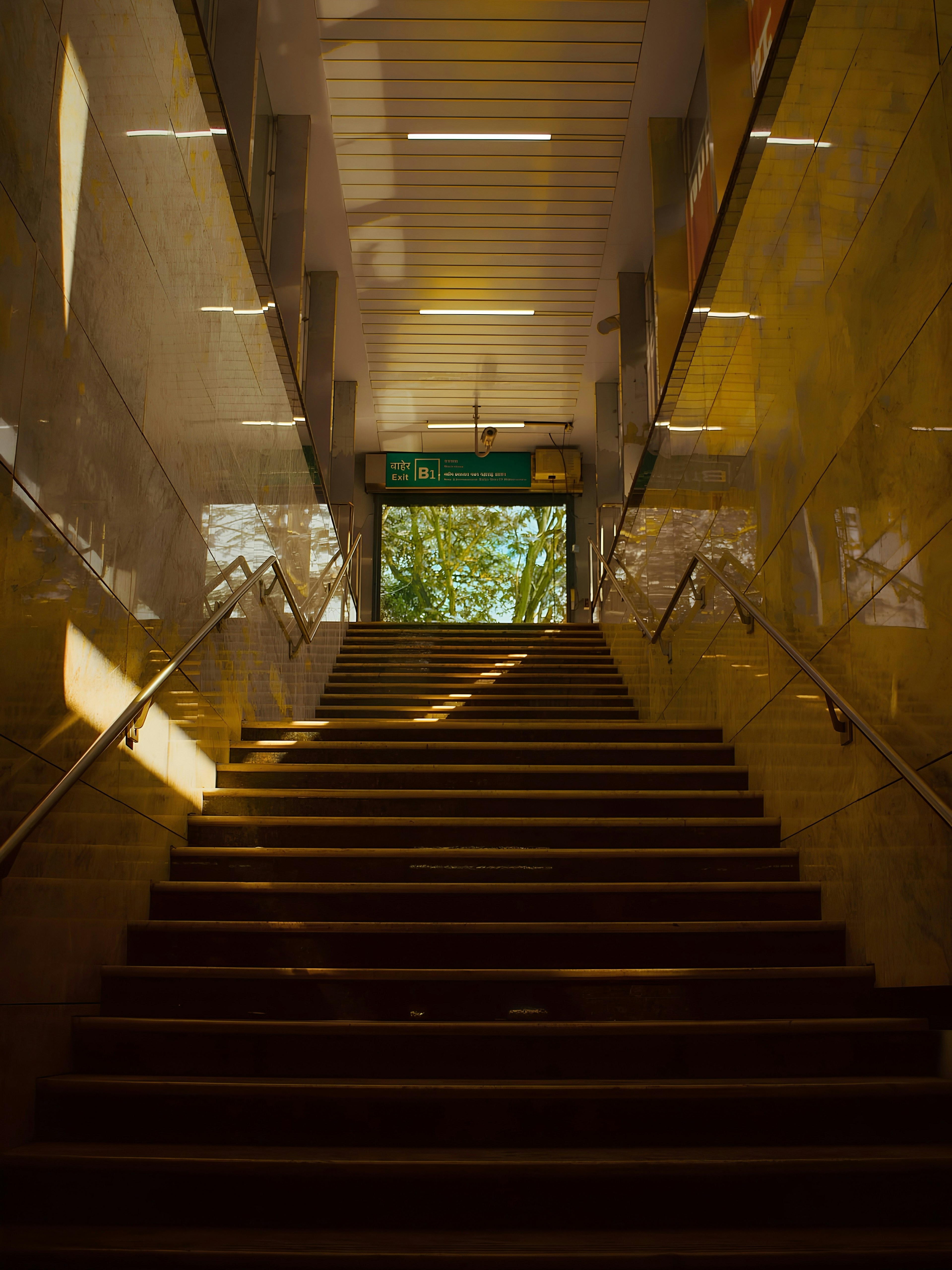 Staircase leading to an exit sign with trees visible through the doorway