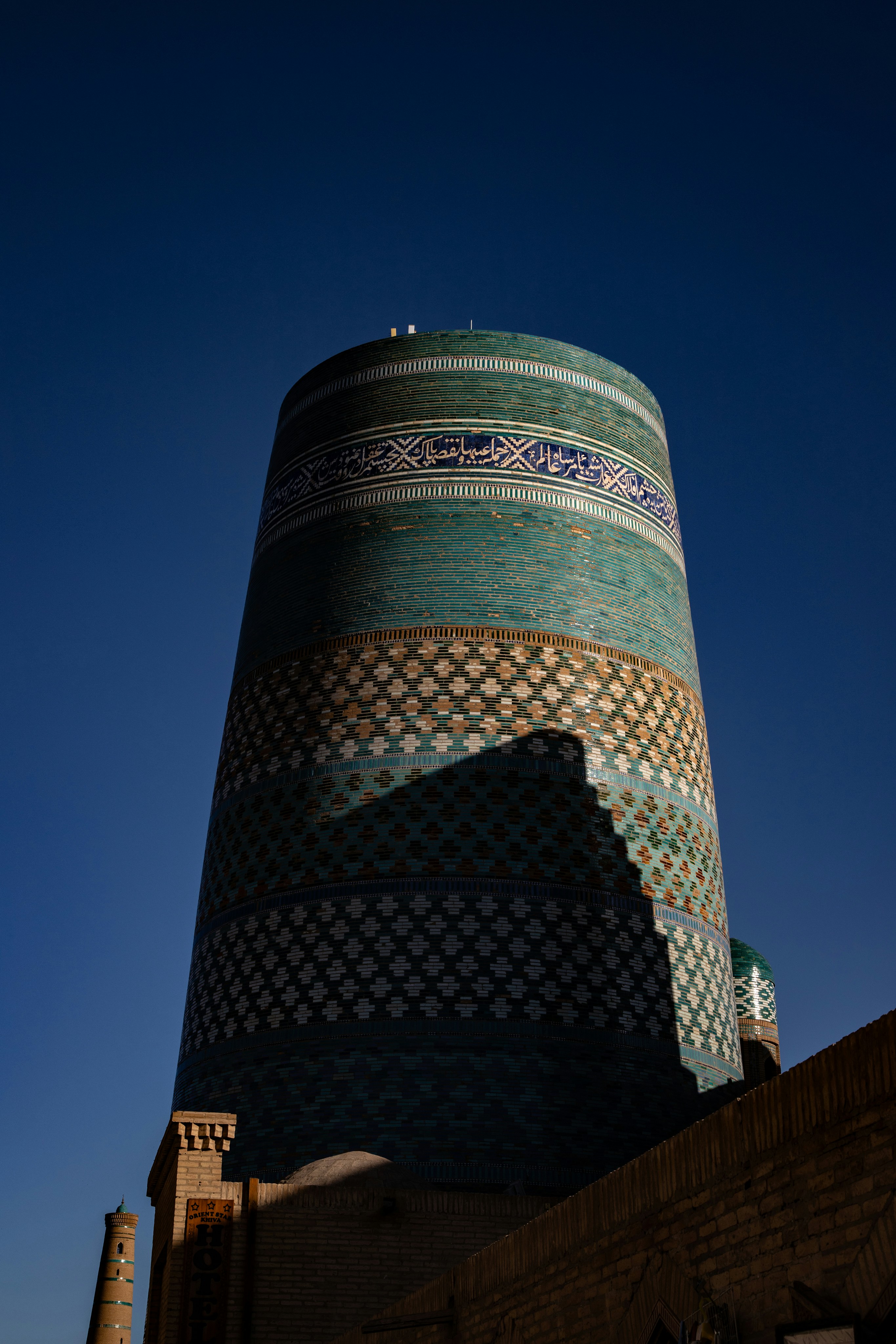 O Minarete de Kalta Menor com azulejos geométricos azuis e verdes contra um céu azul profundo