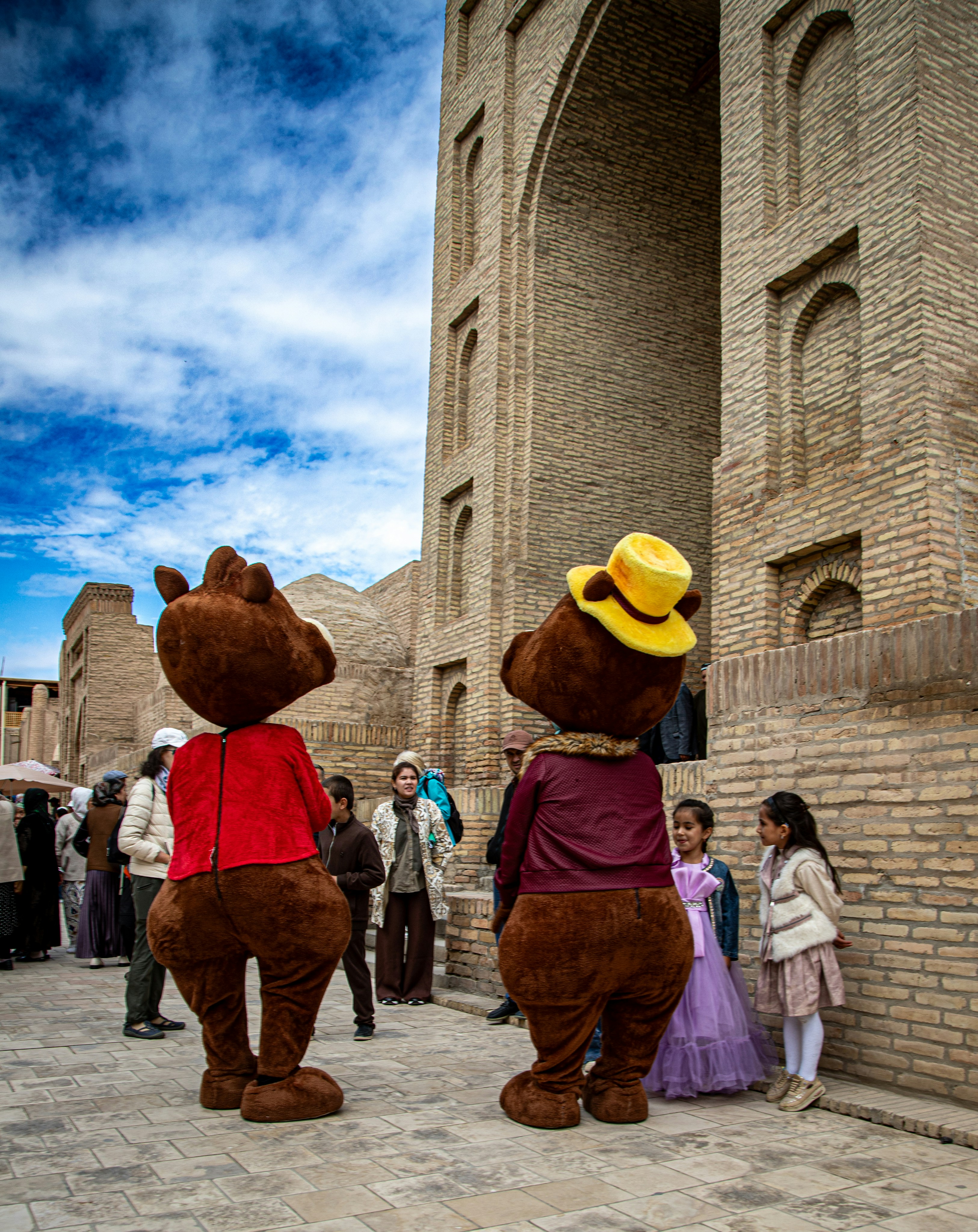 Duas pessoas fantasiadas de urso marrom em pé diante de um grande arco de tijolos