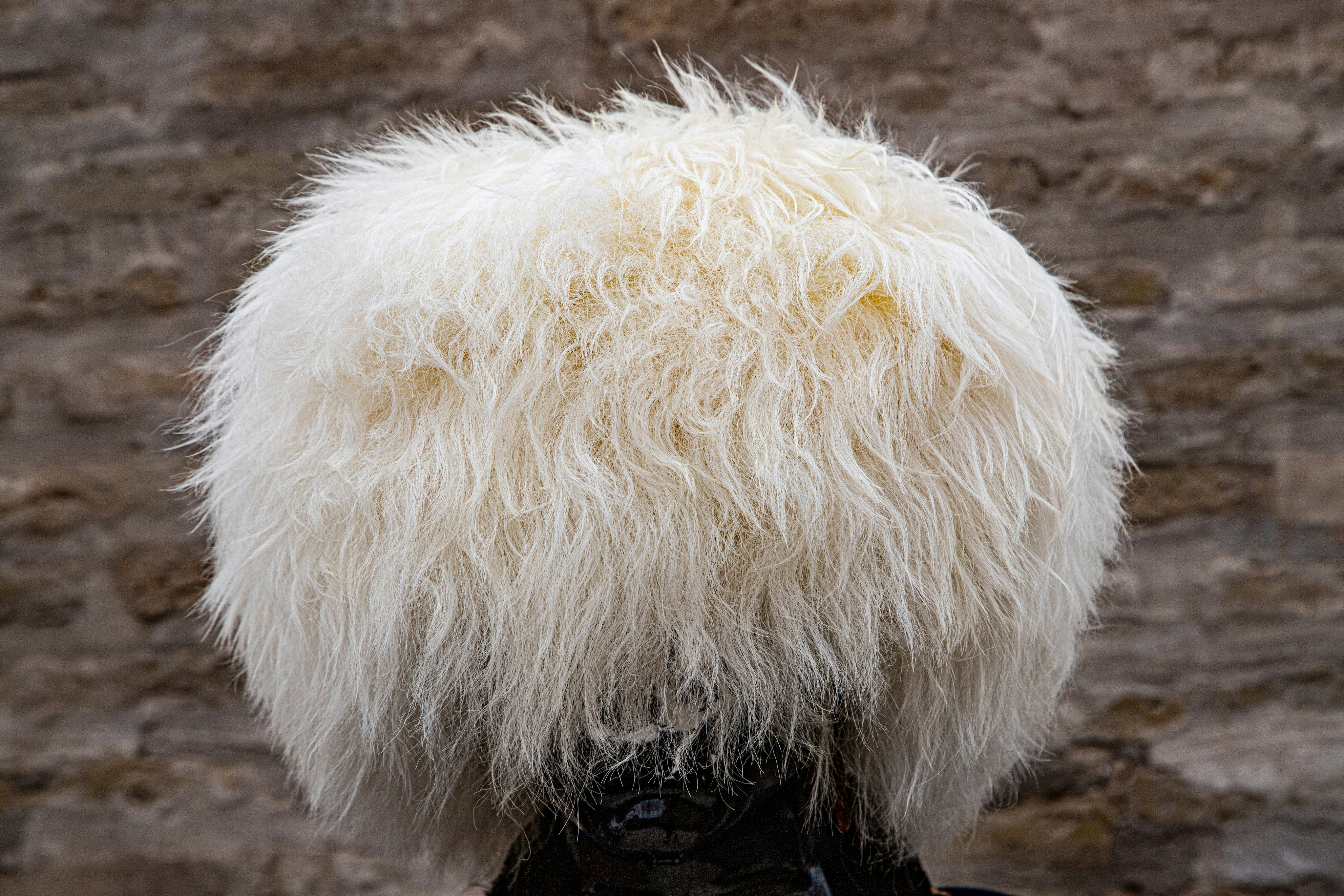 Um chapéu papakha branco e fofo de pele de carneiro contra uma parede de pedra borrada