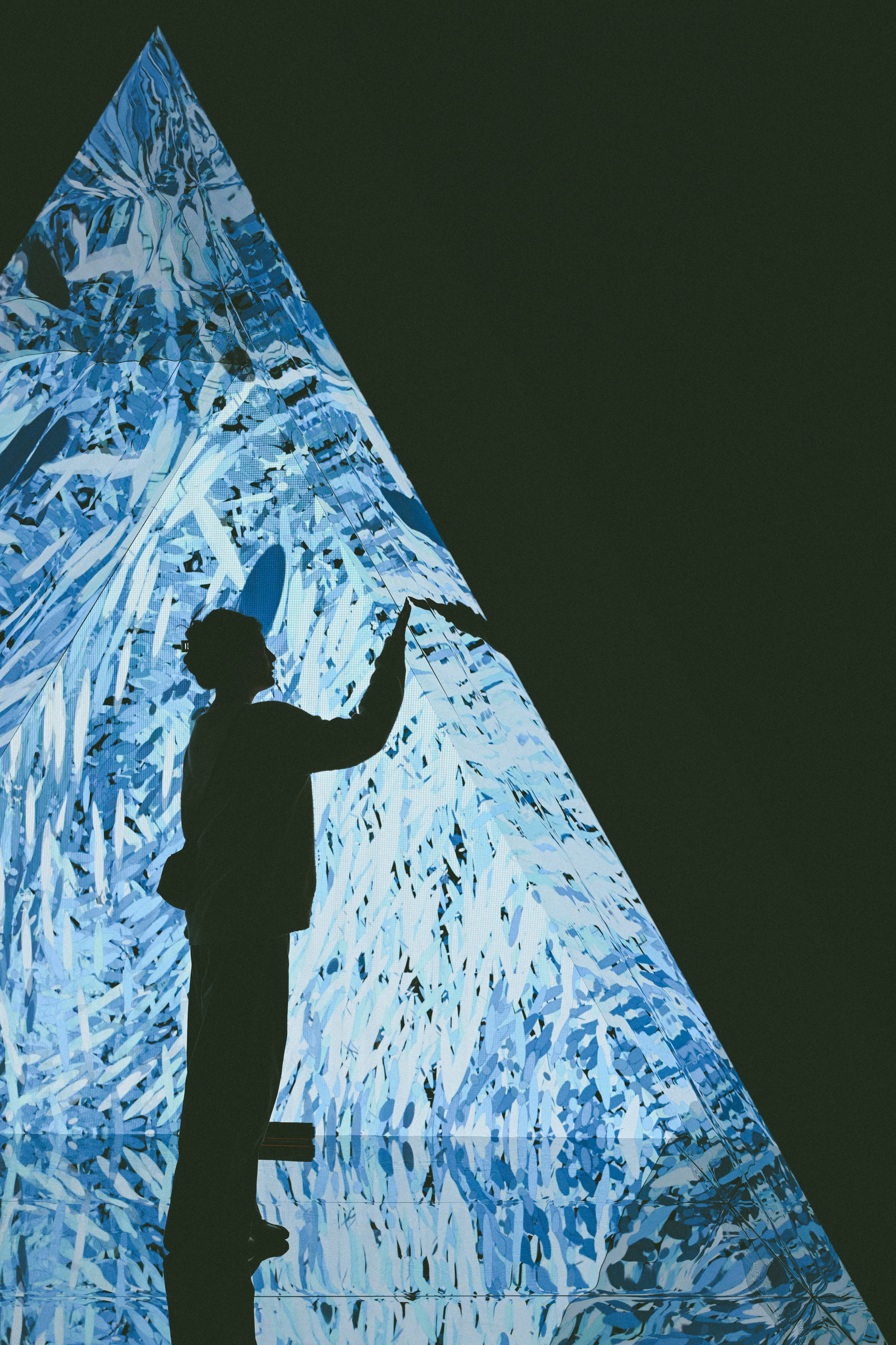 A person in silhouette touching a large glowing blue pyramid display