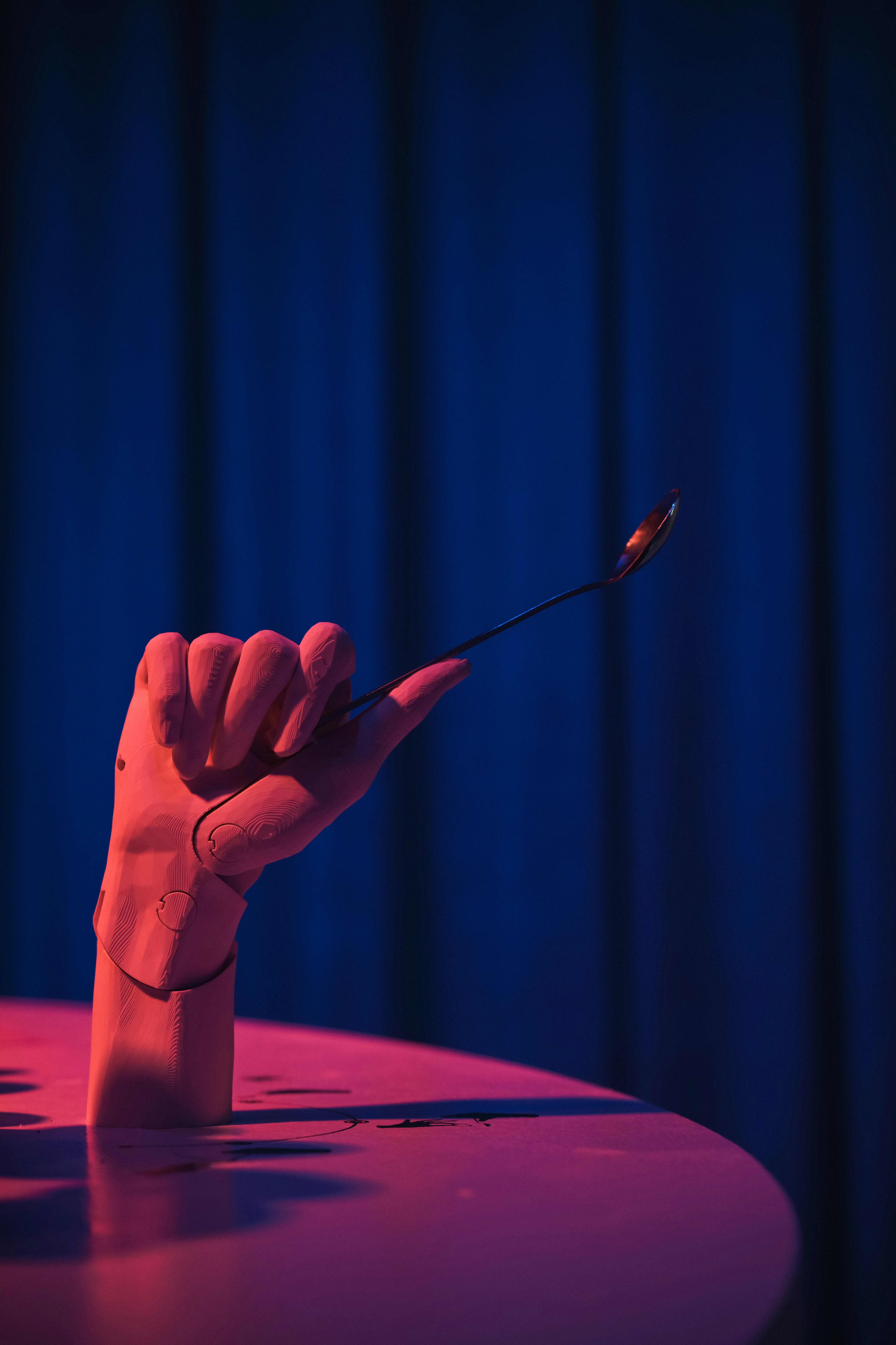 A pink articulated mannequin hand holding a metal spoon on a table