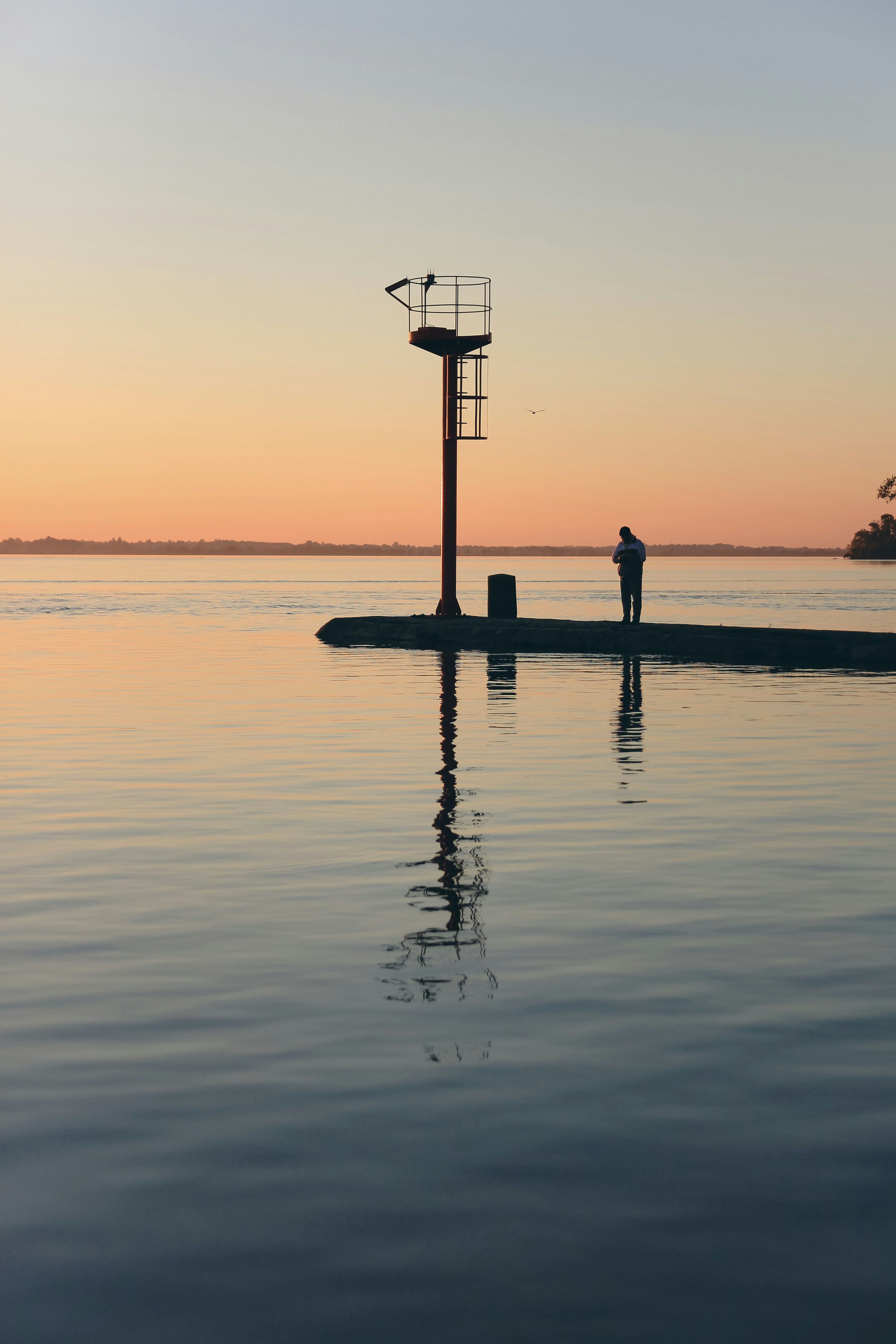 A person in silhouette on a pier with a navigation beacon at golden hour