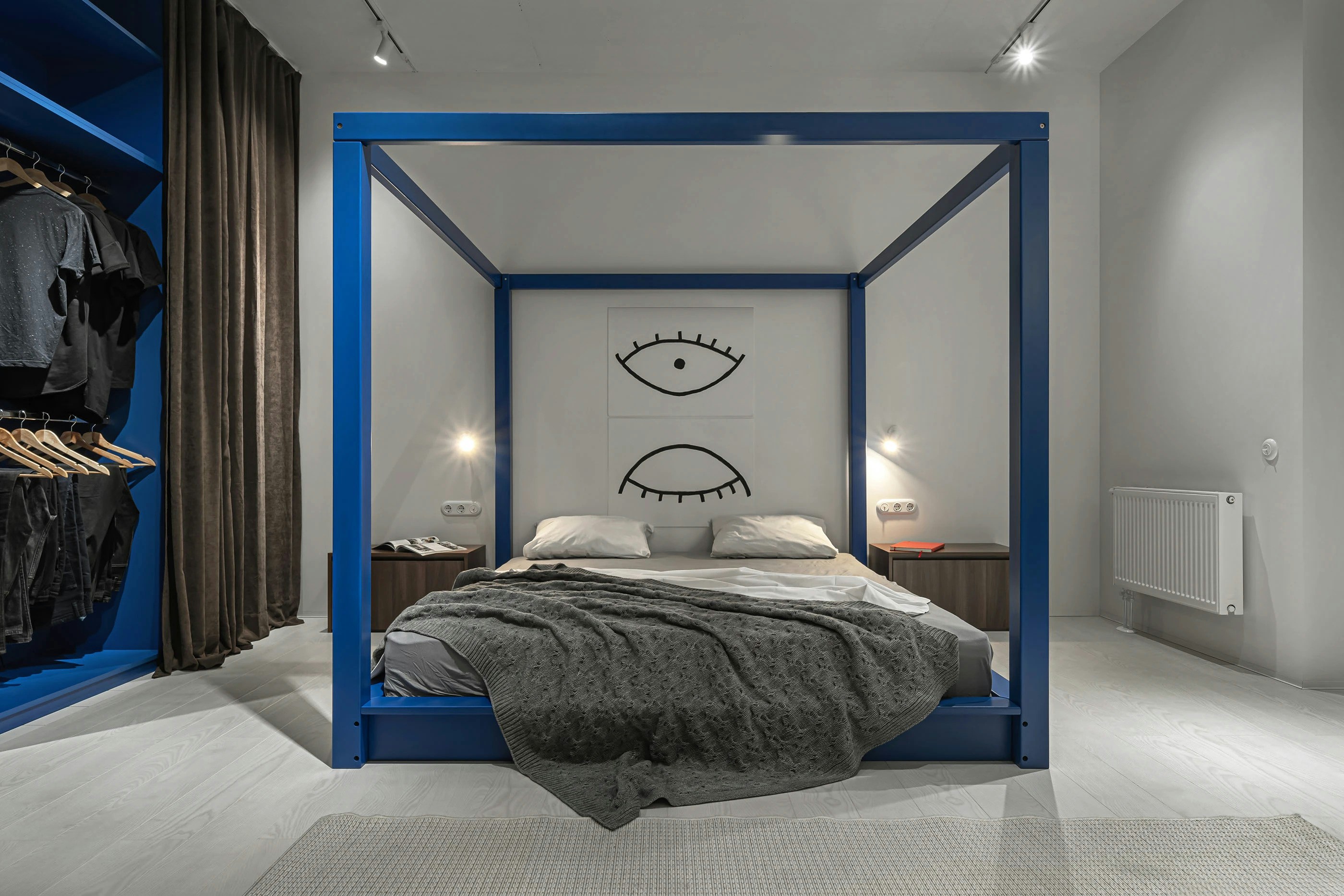 A blue canopy bed with a grey knit blanket in a modern bedroom