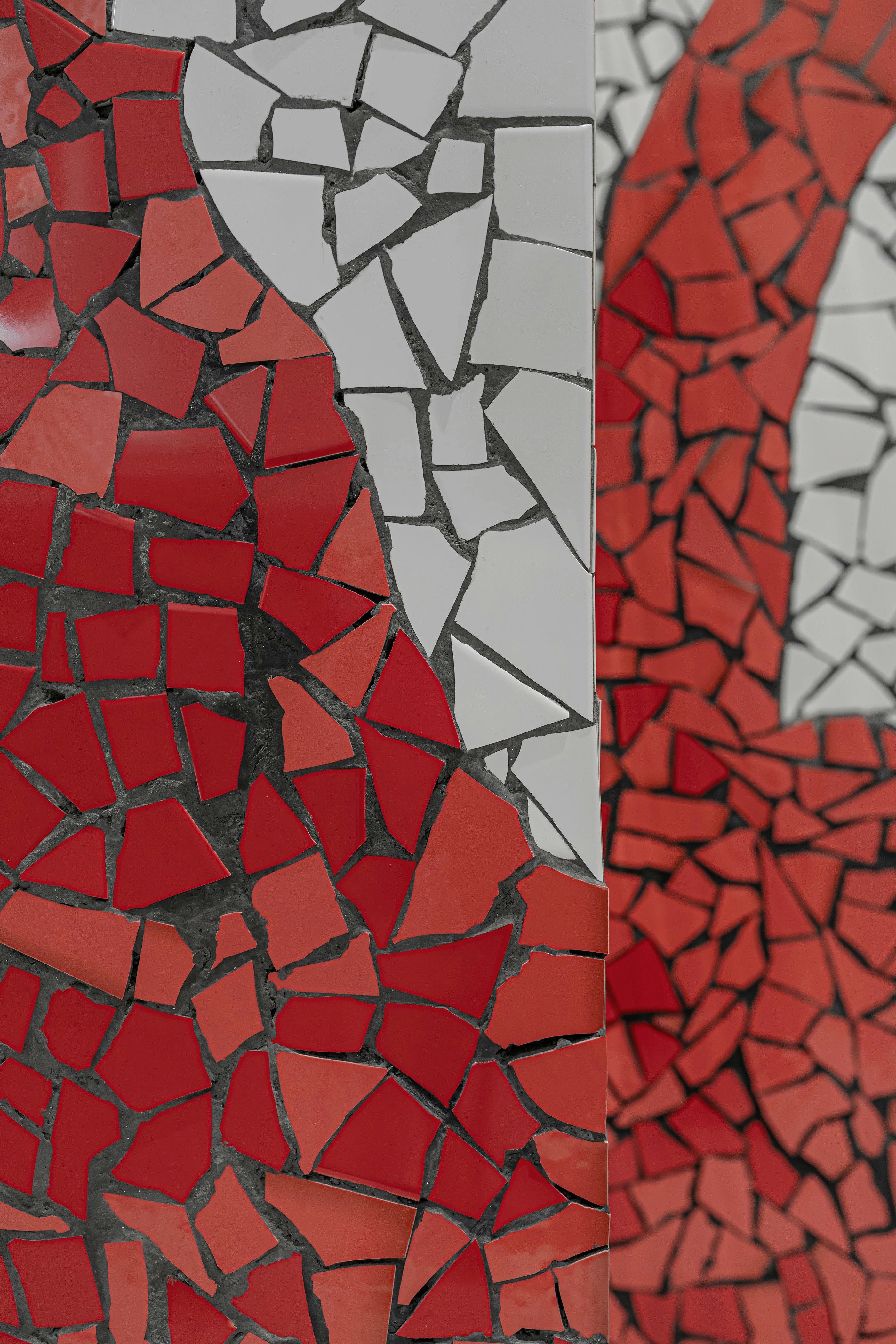 A mosaic of irregular red and white ceramic tiles on a corner wall