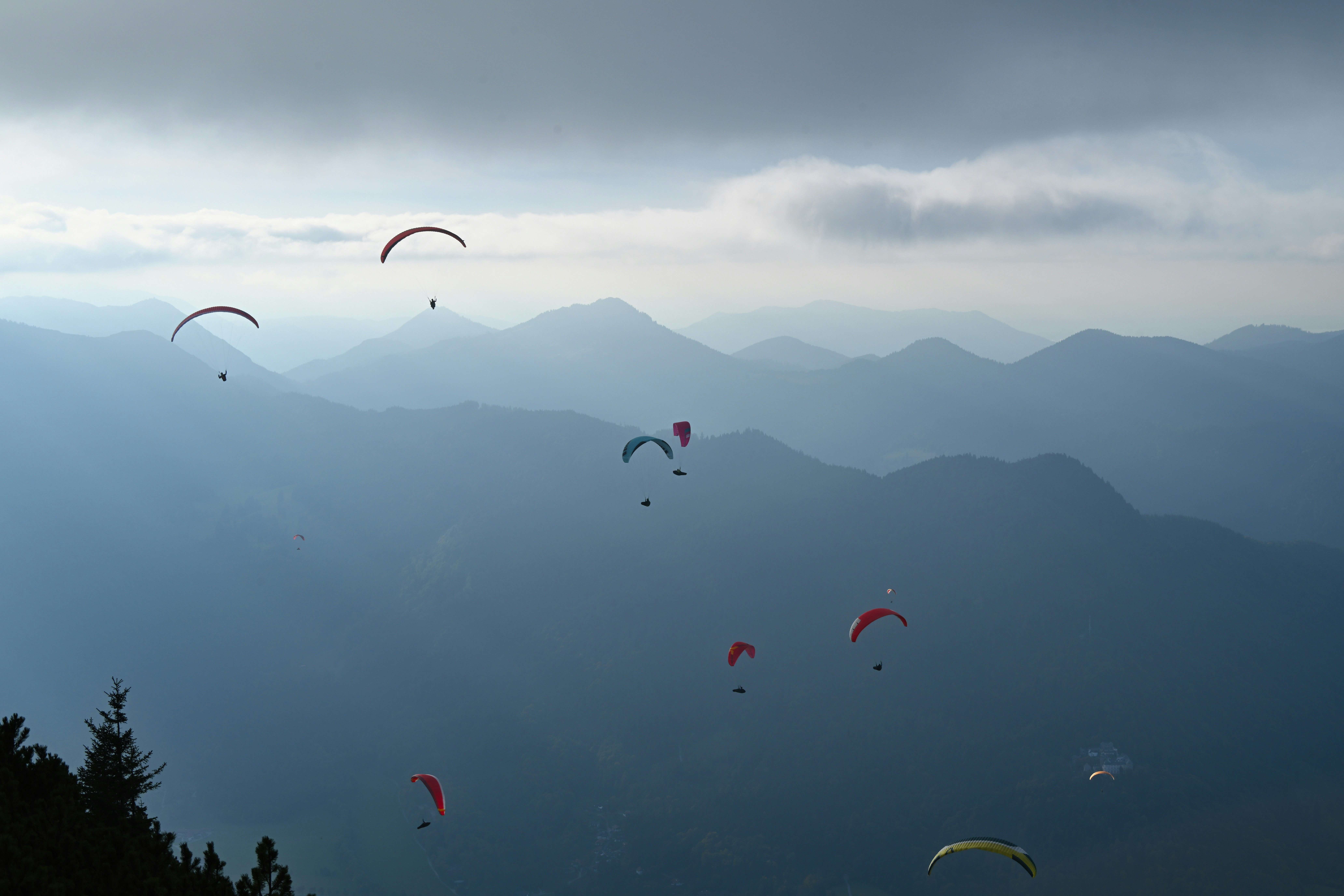 A group of paragliders soaring above misty blue mountain ridges under a cloudy sky