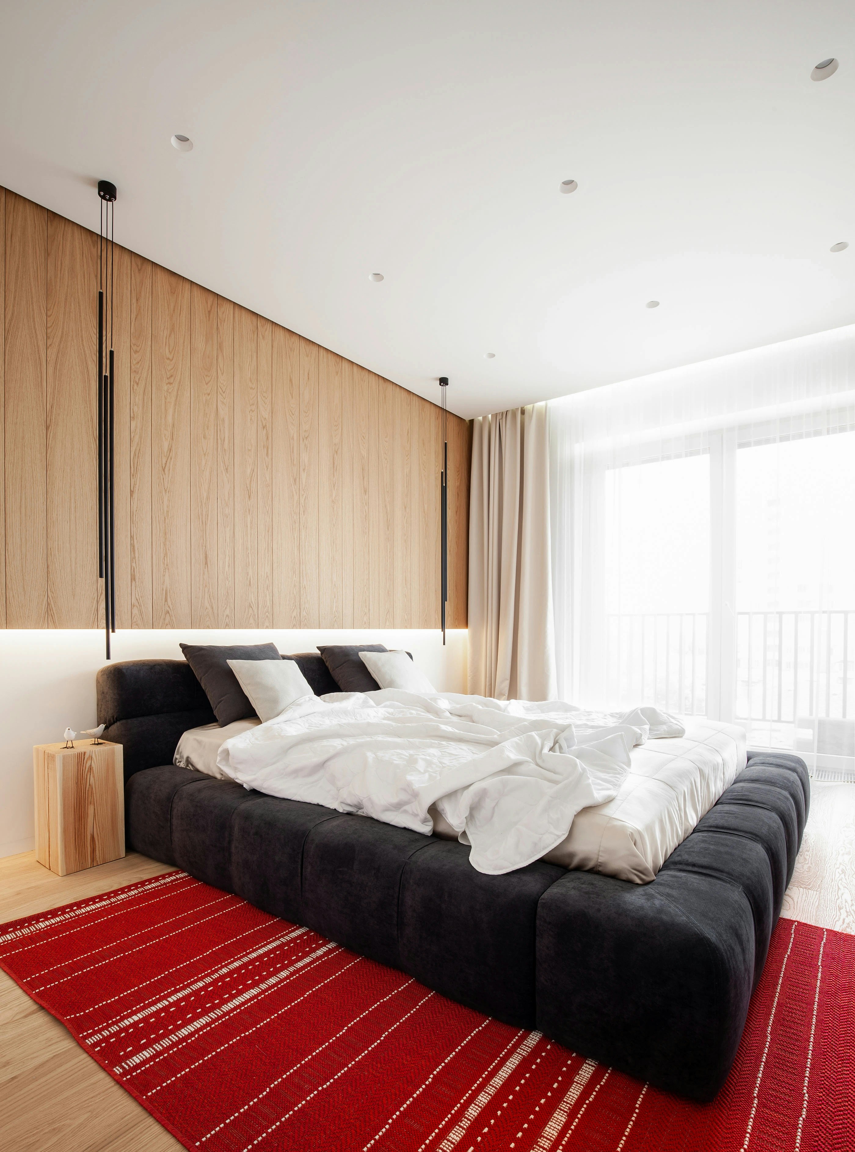 A modern bedroom with a dark upholstered bed and a red rug on wood flooring