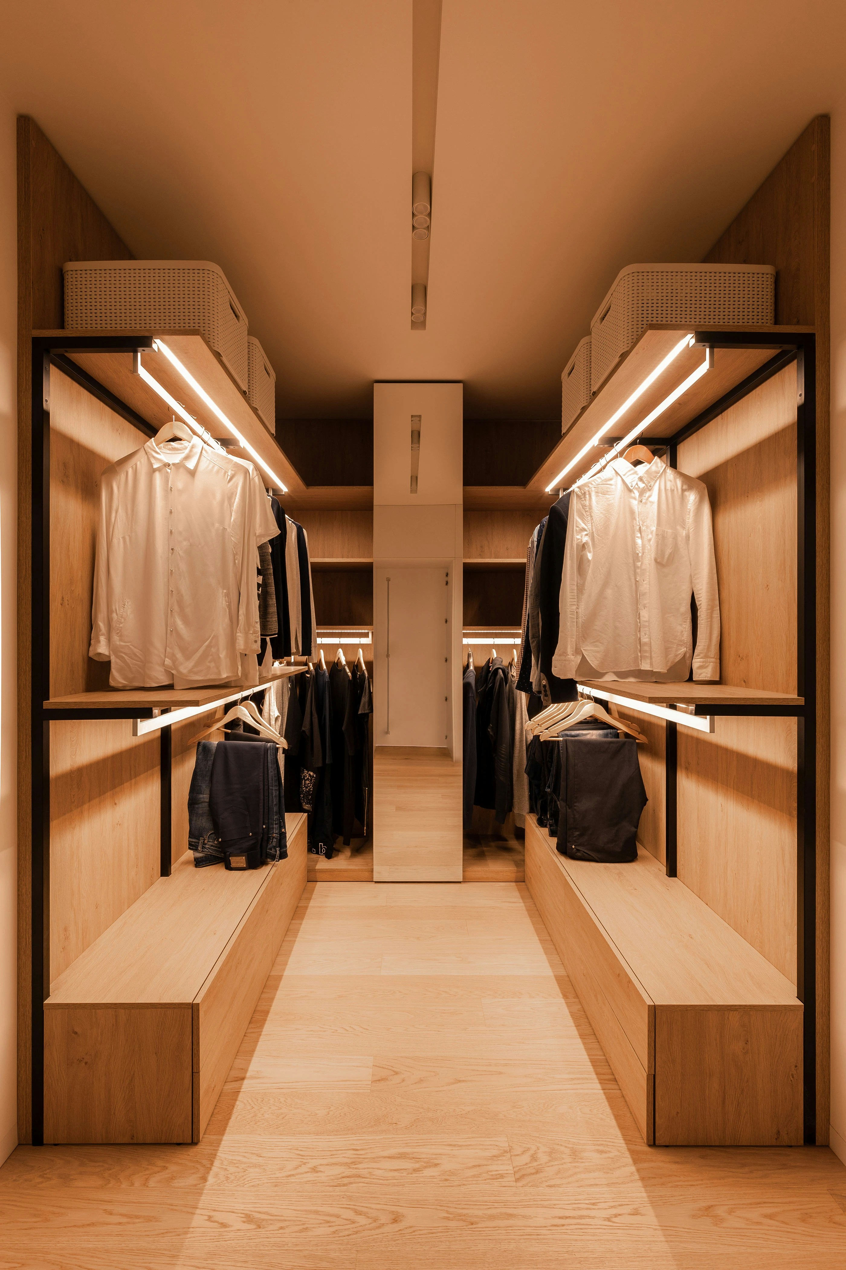 A walk-in closet with wooden shelves, hanging clothes, and integrated warm lighting