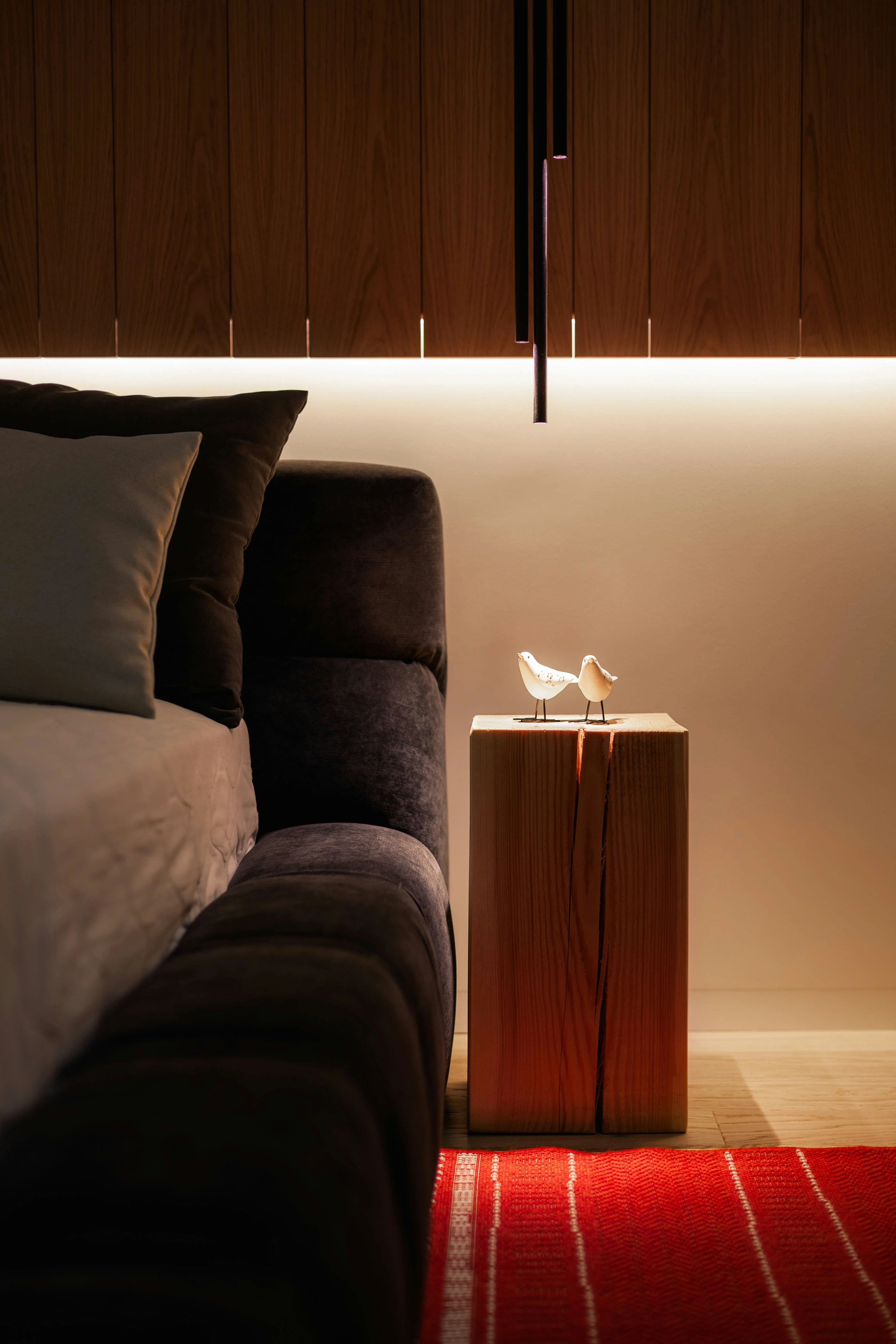 Two small bird figurines on a wooden block beside a dark upholstered bed