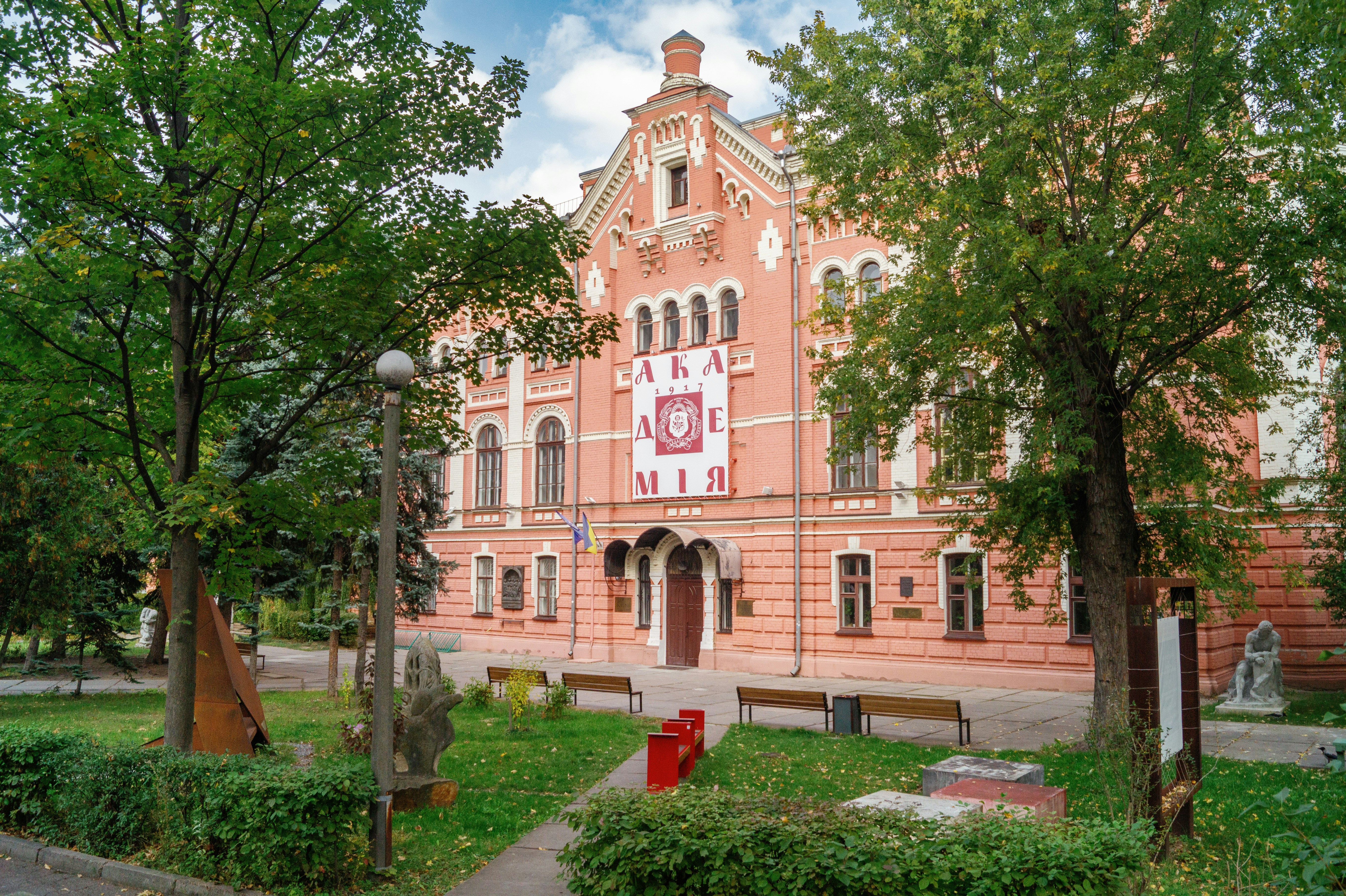 A historic red brick building with a banner reading "АКАДЕМІЯ" in a park