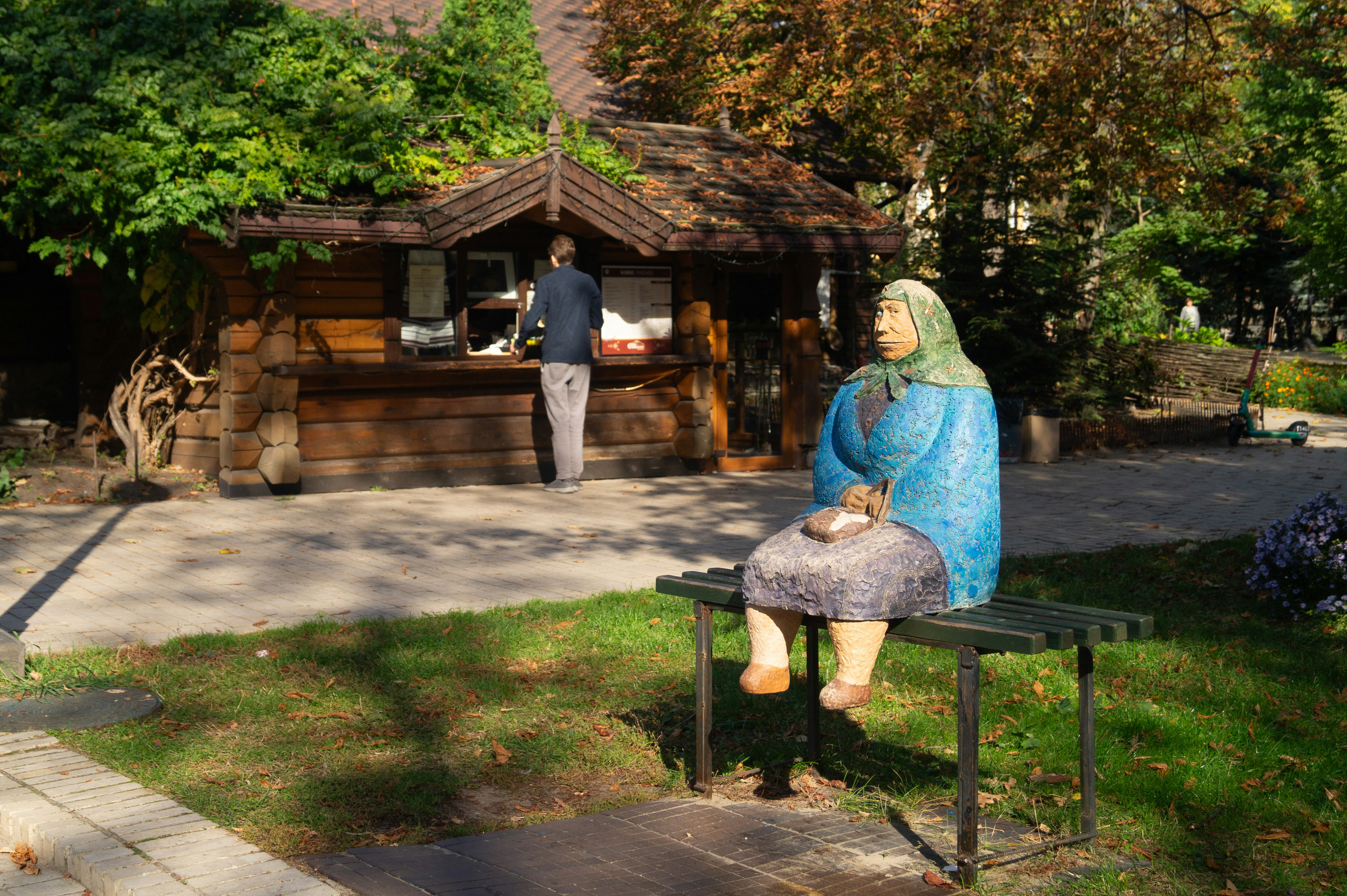 A painted sculpture of an elderly woman in a headscarf on a park bench