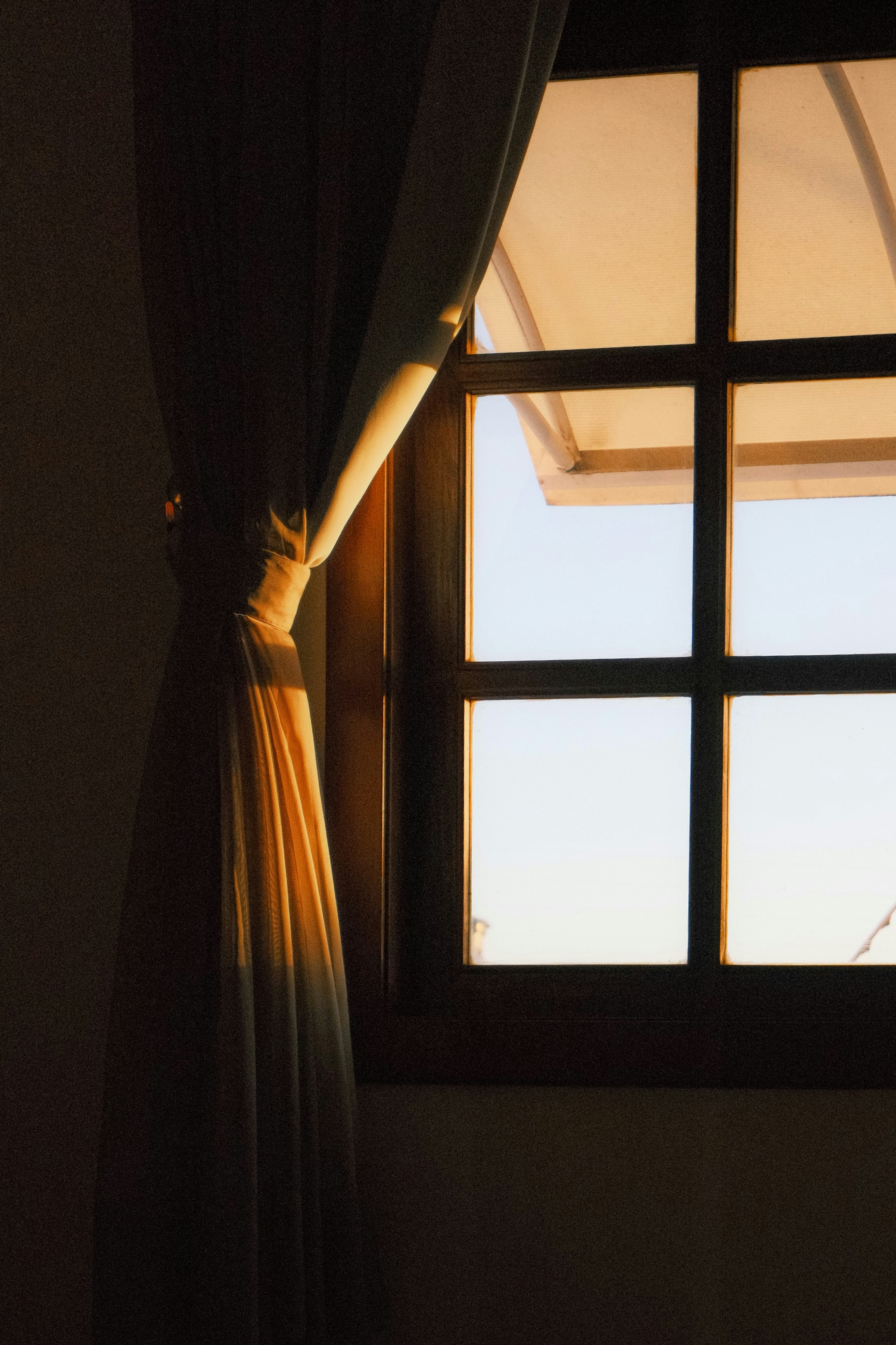 A window with a wooden frame and a curtain in warm golden light