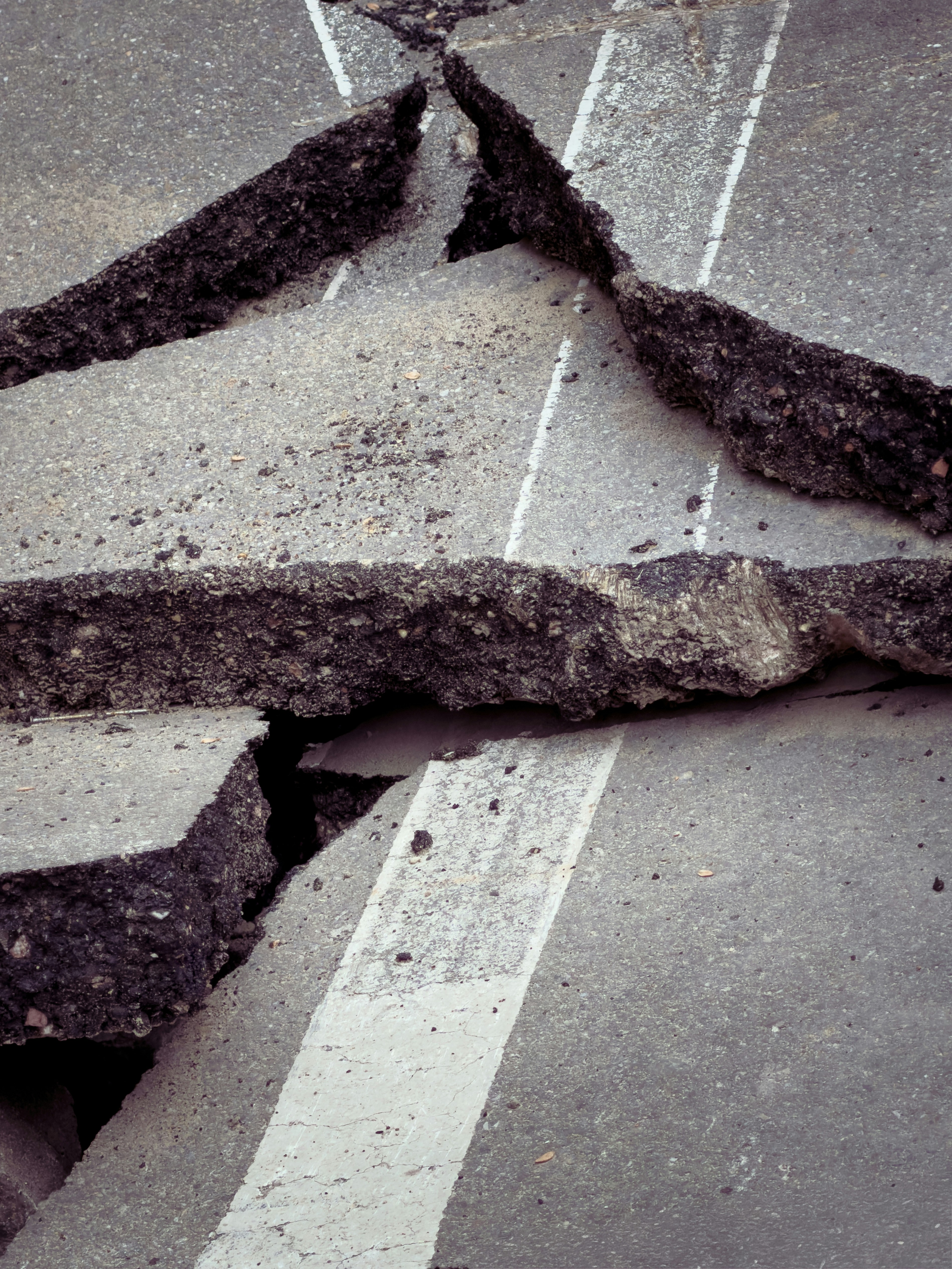 Cracked asphalt road surface with white lane markings and deep fissures