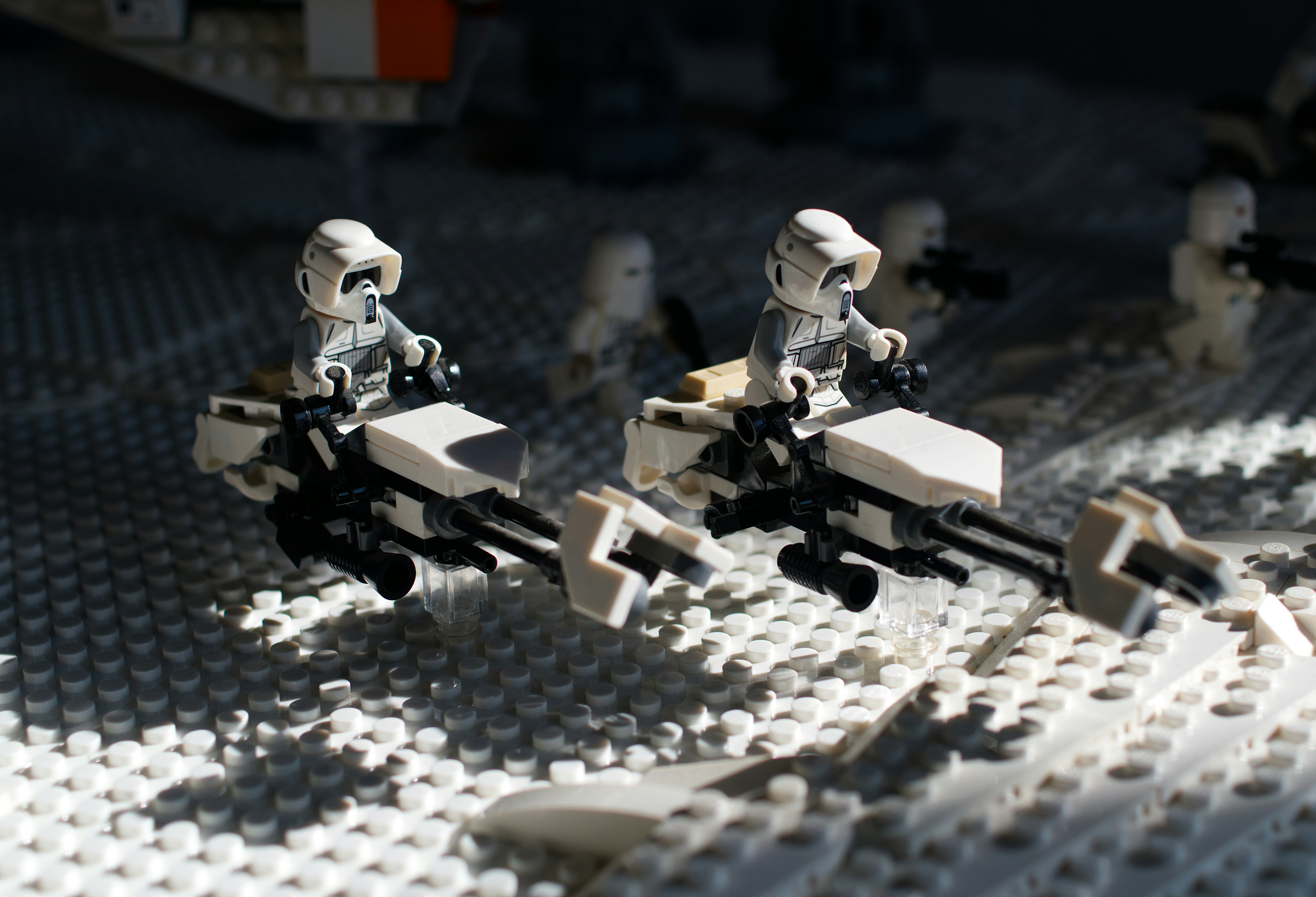 Two Lego scout troopers on speeder bikes over a white studded baseplate