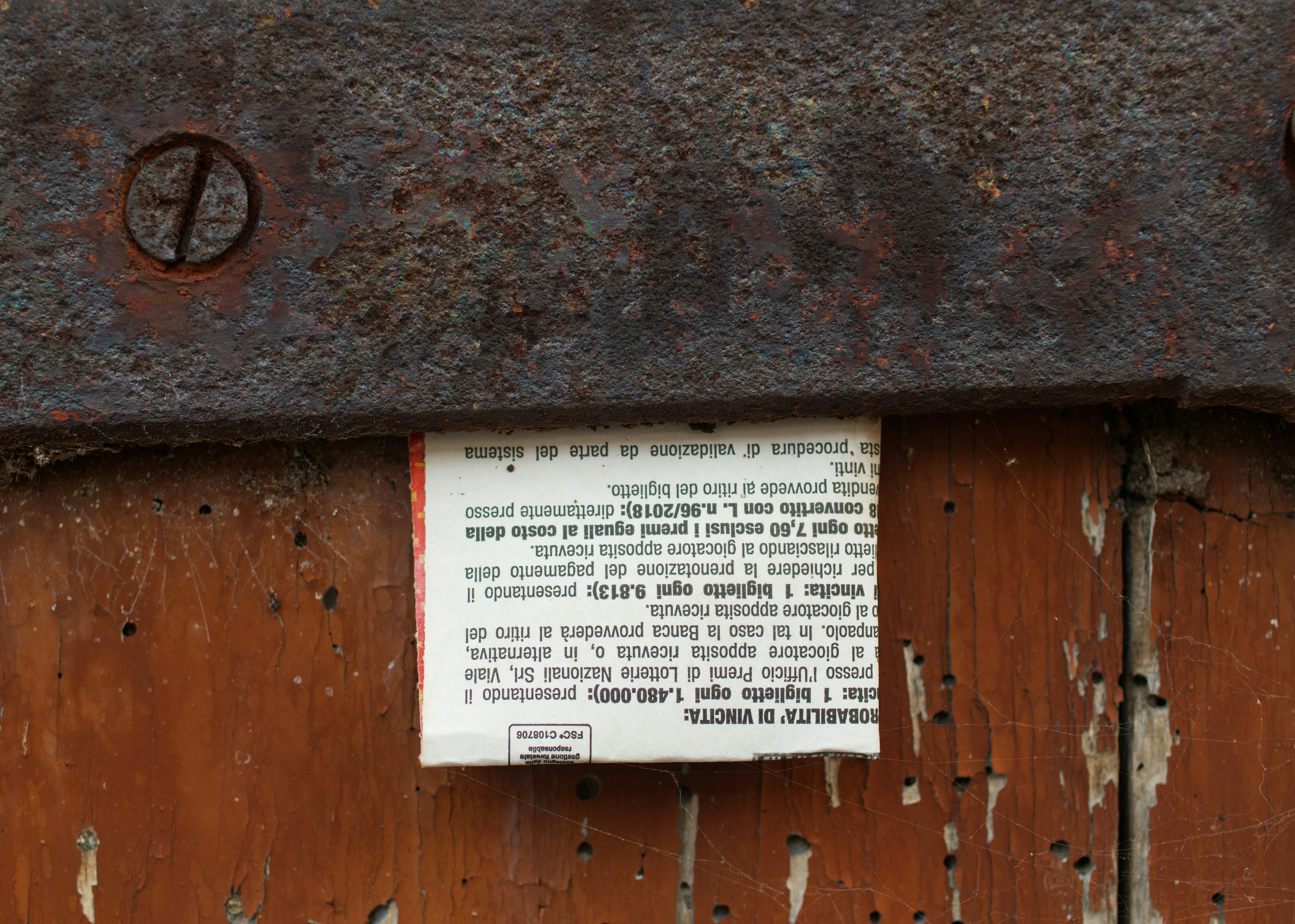 A piece of paper with Italian text tucked under a rusted metal hinge