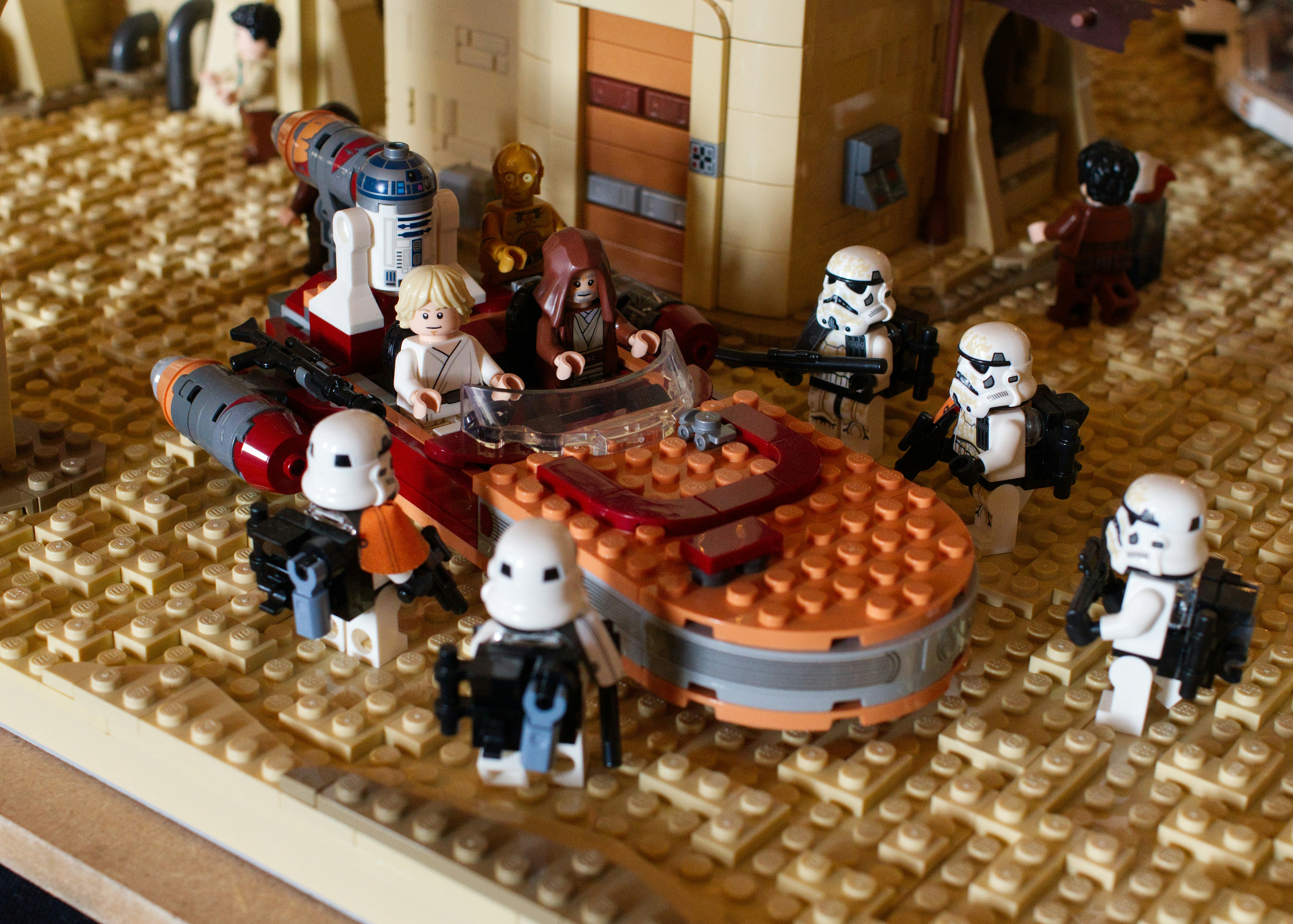 Lego Star Wars minifigures in a landspeeder surrounded by stormtroopers on a desert base