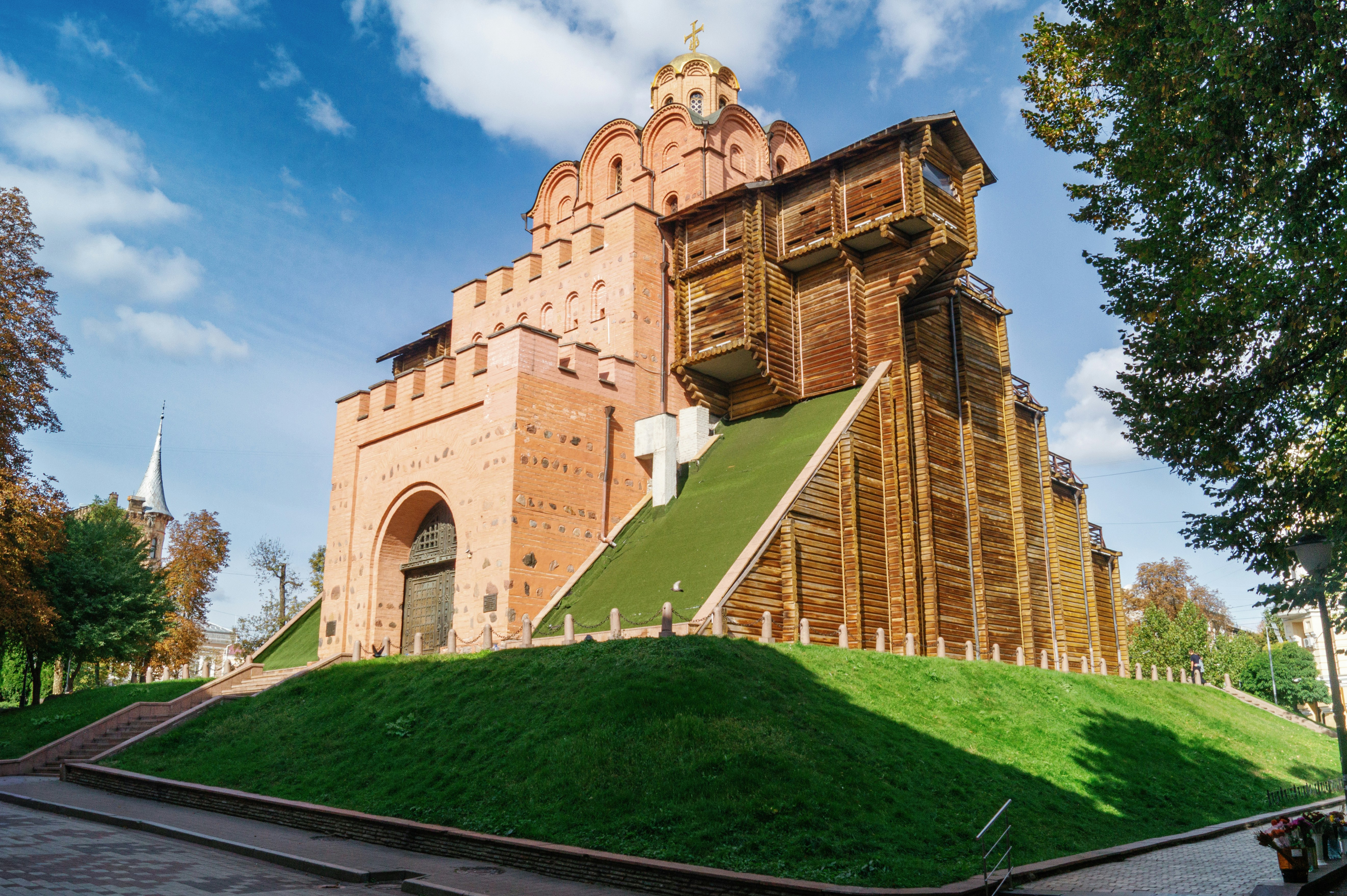 A large brick gatehouse with wooden ramparts on a grassy hill under a blue sky