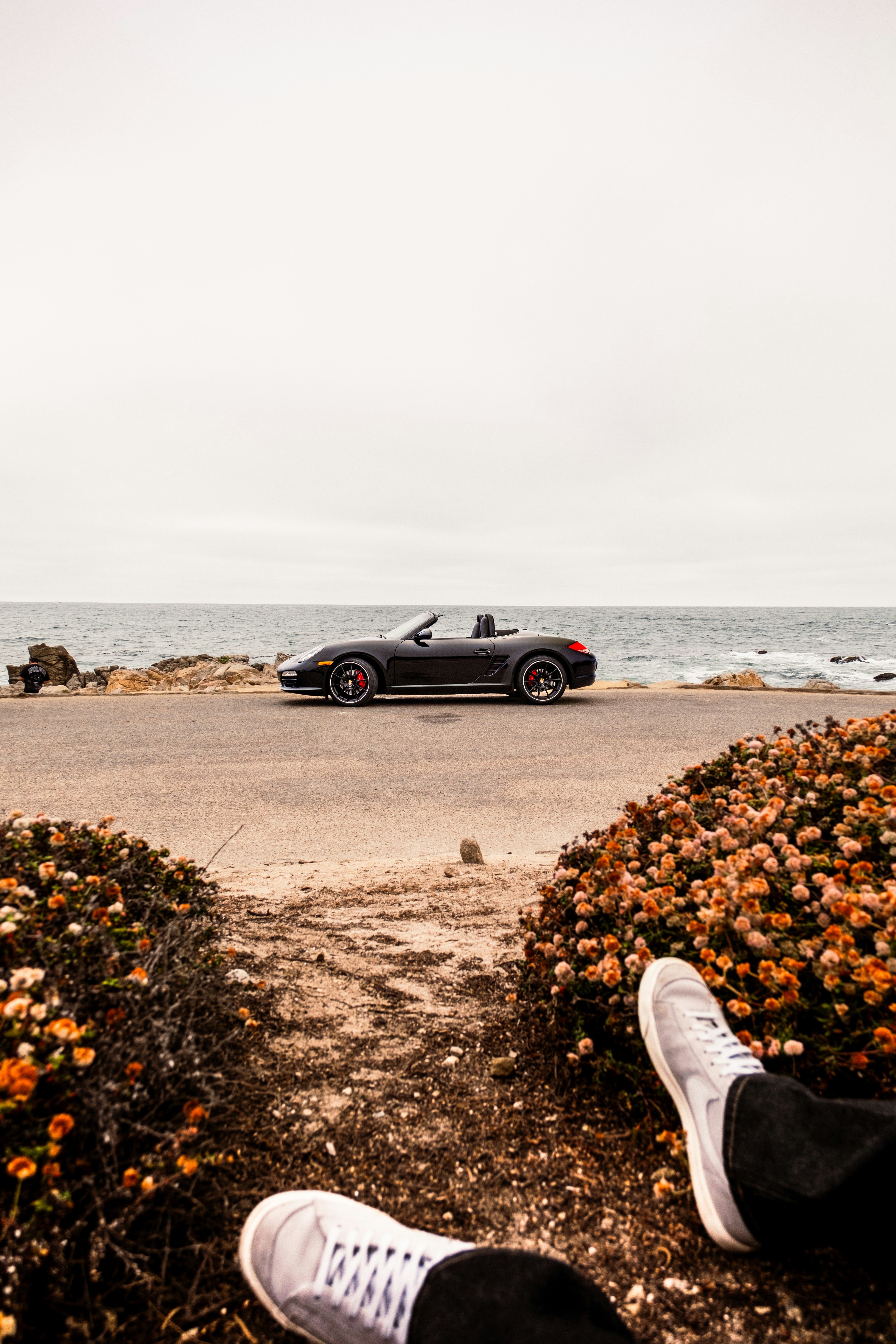 A black convertible sports car parked on a coastal road by the ocean