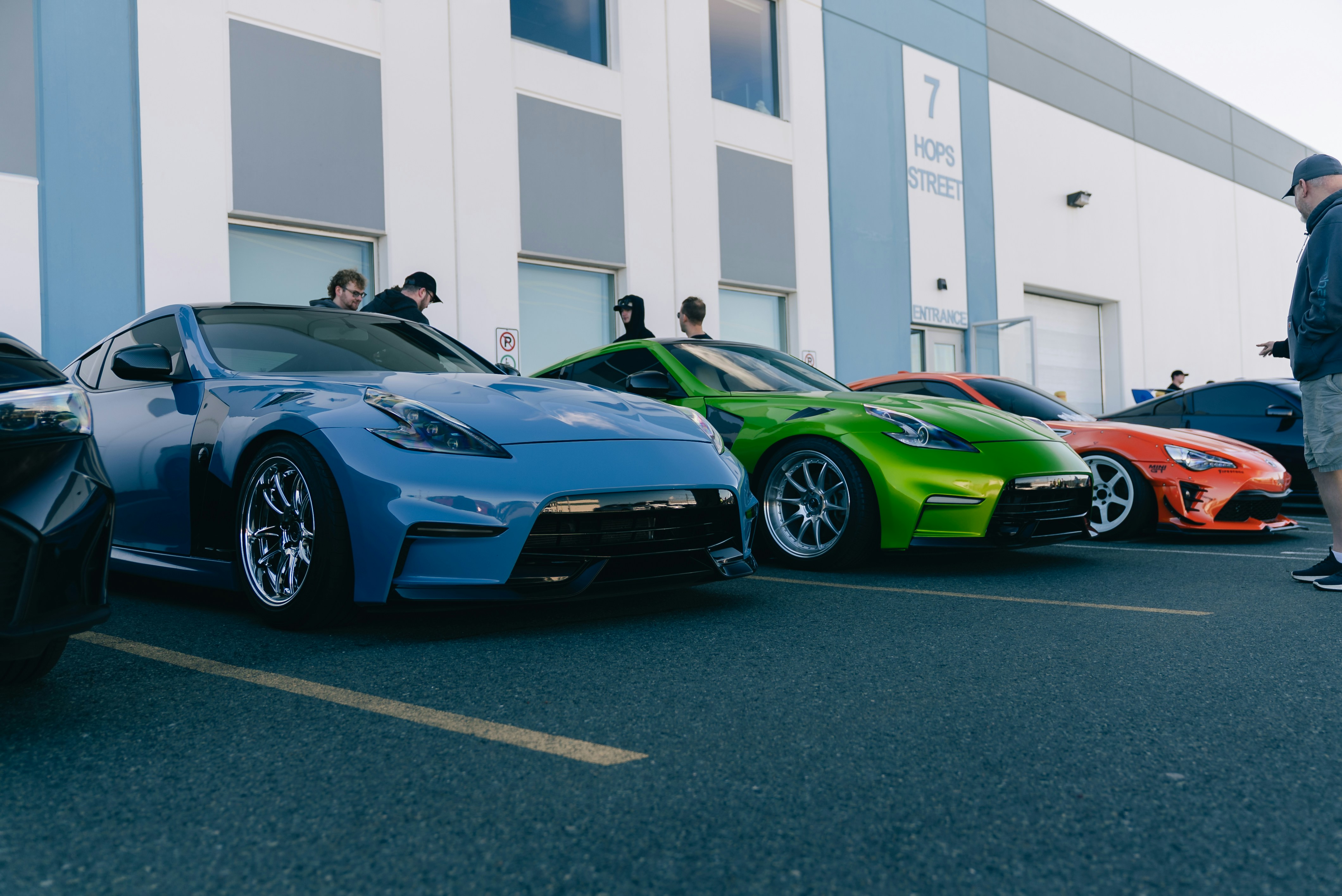 A blue and a green sports car parked in front of a warehouse building