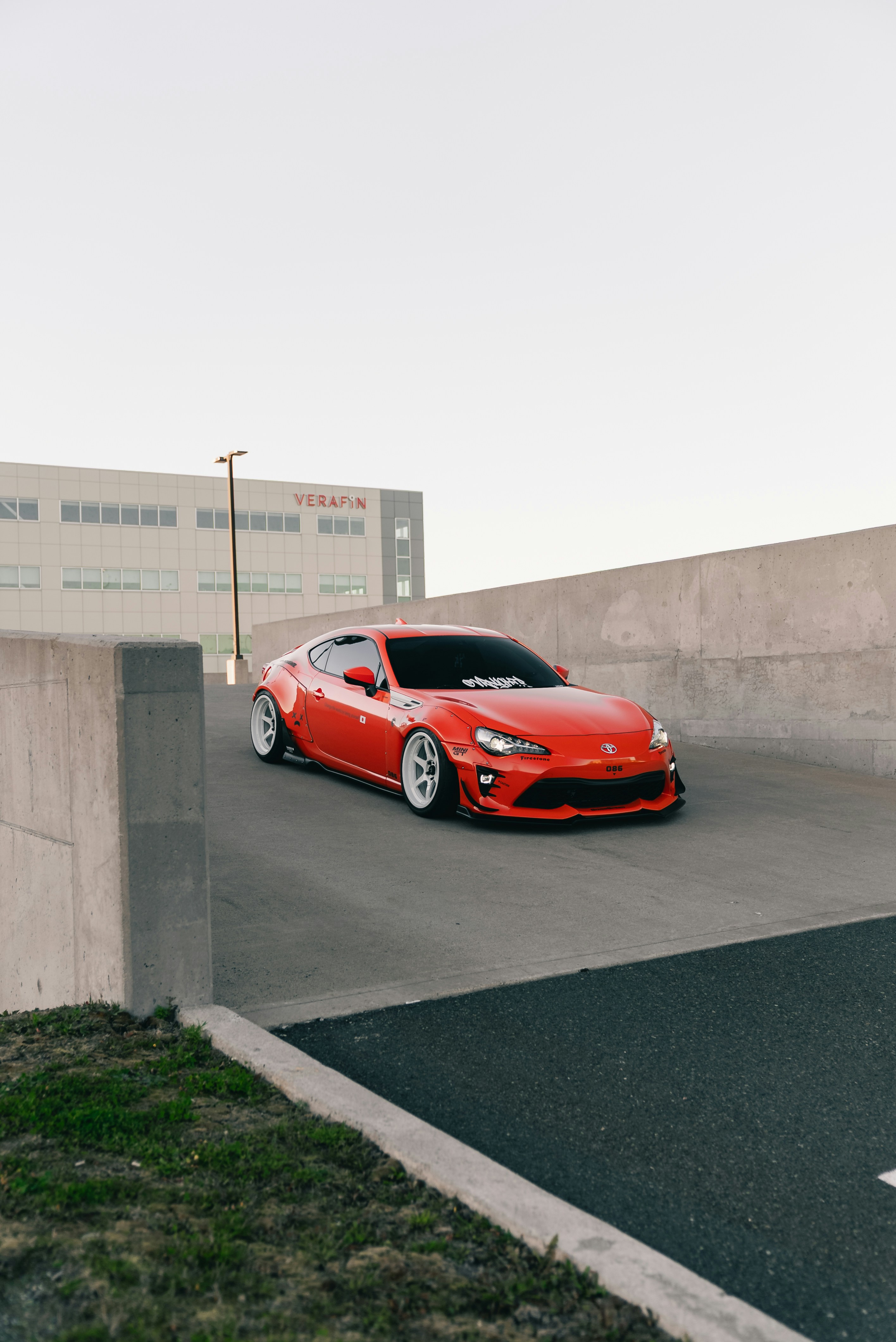 A modified orange Toyota 86 sports car on a concrete parking garage ramp