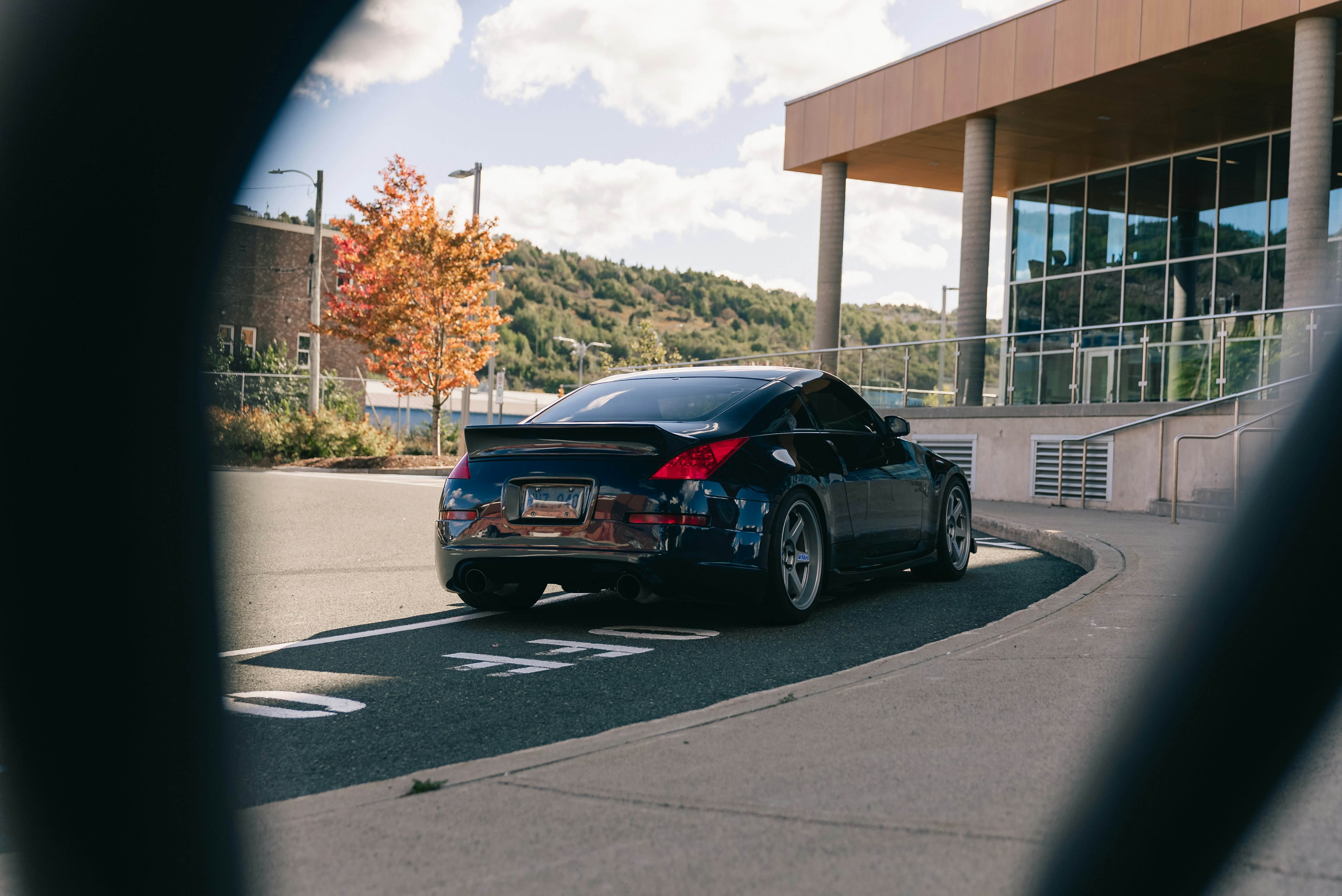Un Nissan 350Z azul oscuro aparcado en asfalto cerca de un edificio moderno
